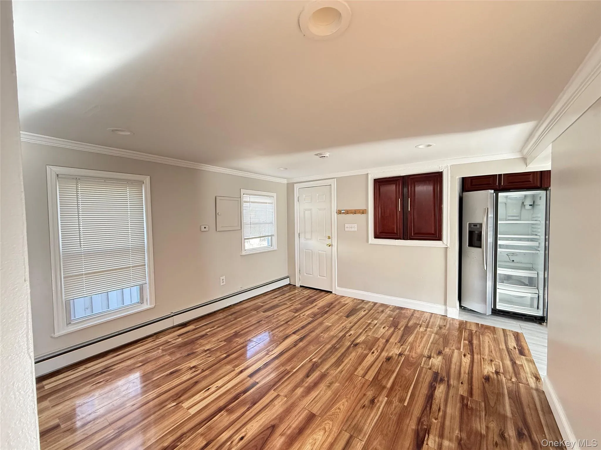 Unfurnished room with baseboard heating, light wood-style flooring, and ornamental molding Unfurnished room with baseboard heating, light wood-style flooring, and ornamental molding