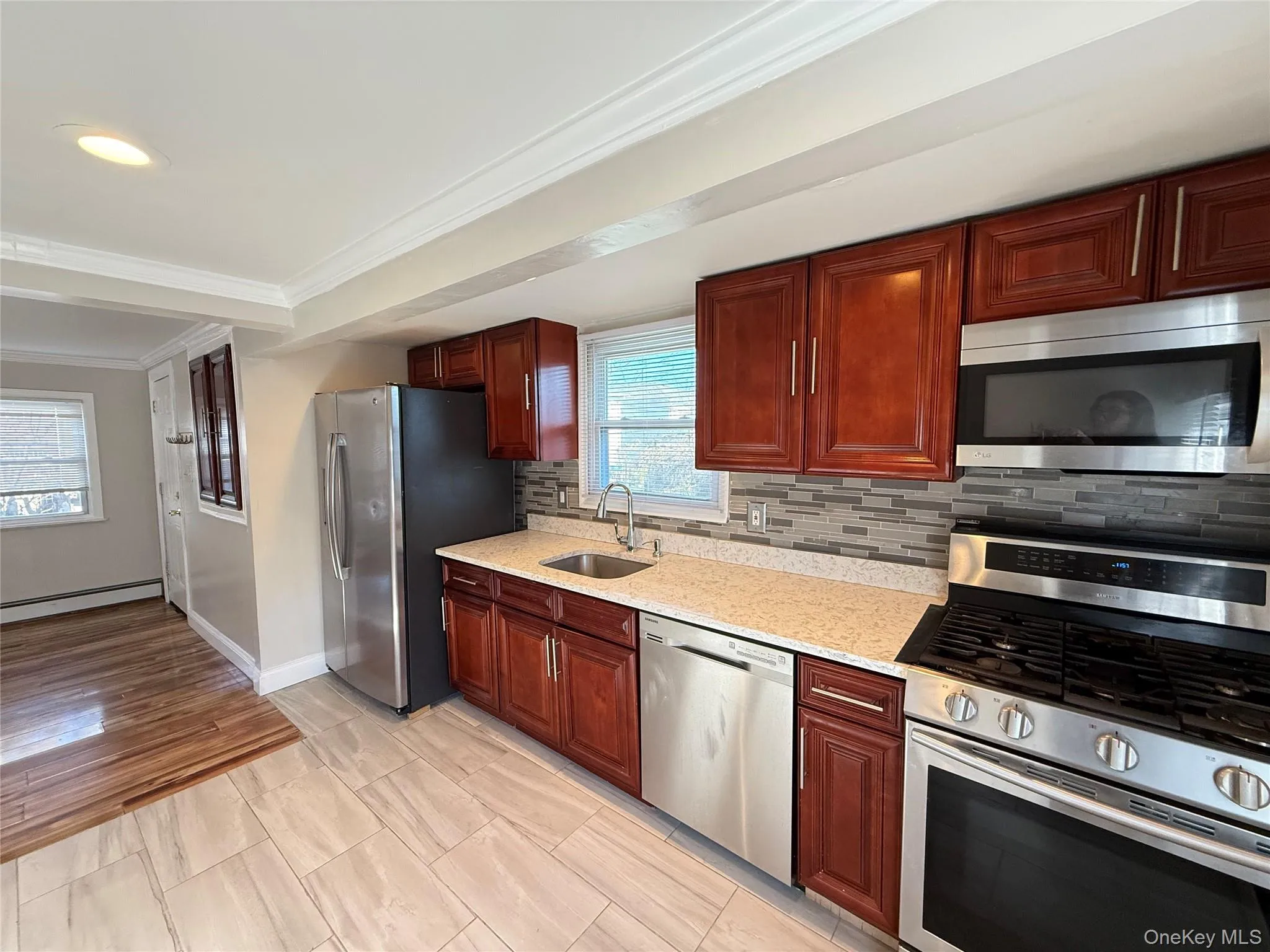 Kitchen featuring stainless steel appliances, crown molding, light stone counters, dark brown cabinets, and baseboard heating Kitchen featuring stainless steel appliances, crown molding, light stone counters, dark brown cabinets, and baseboard heating