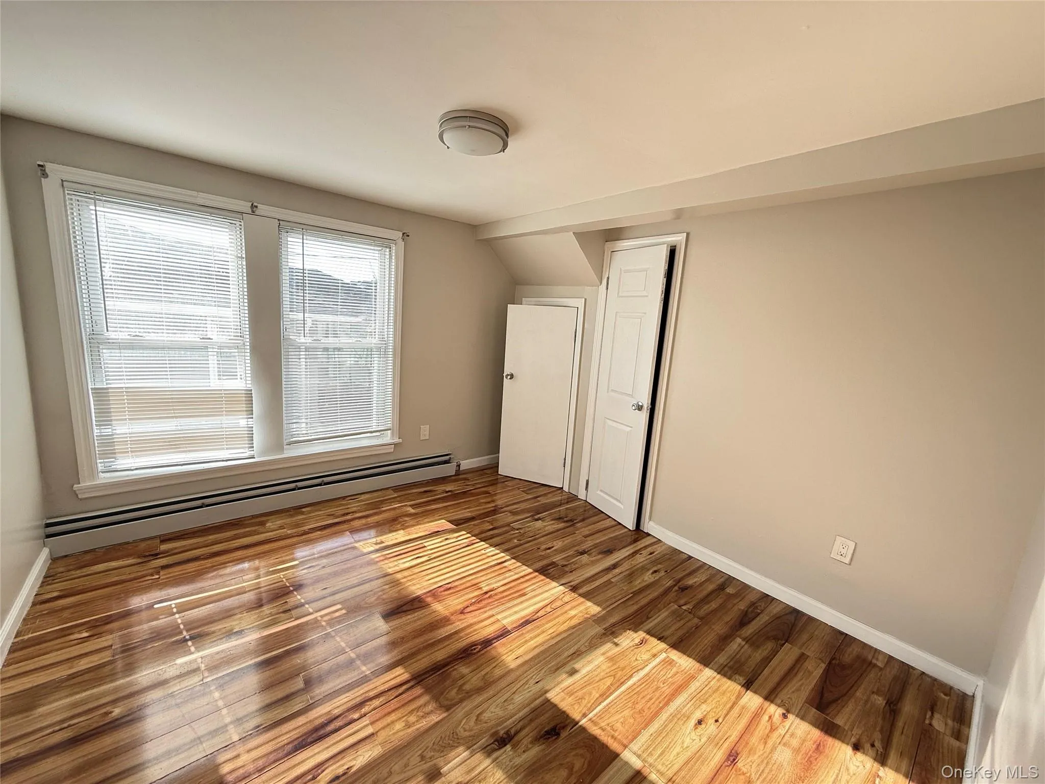 Unfurnished bedroom featuring a baseboard radiator and wood finished floors Unfurnished bedroom featuring a baseboard radiator and wood finished floors