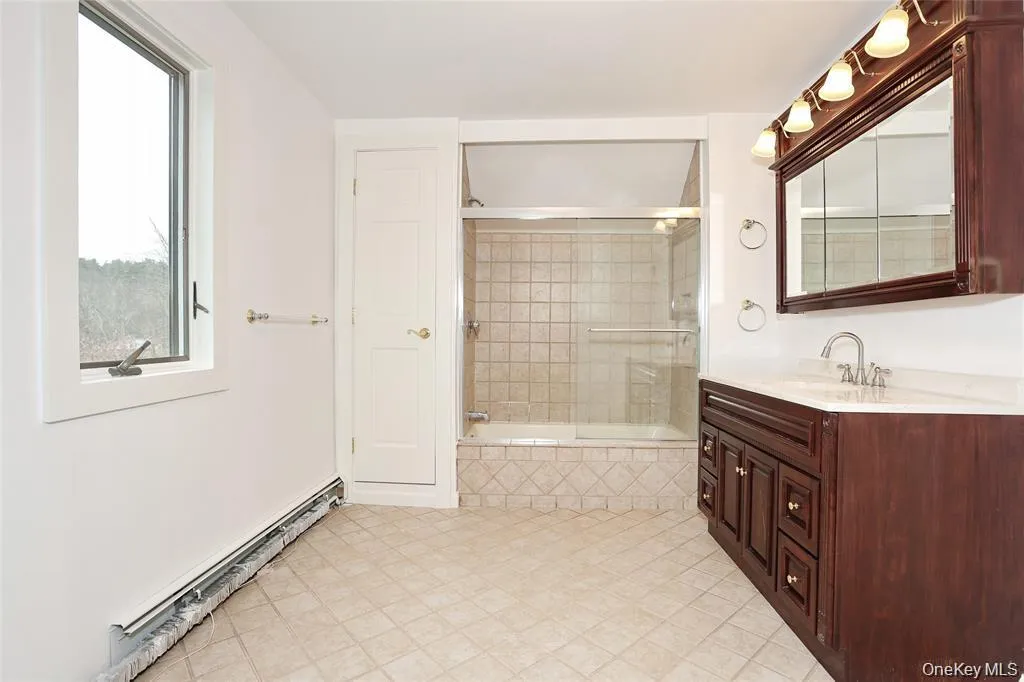 Bathroom featuring baseboard heating, vanity, and tiled shower / bath Bathroom featuring baseboard heating, vanity, and tiled shower / bath