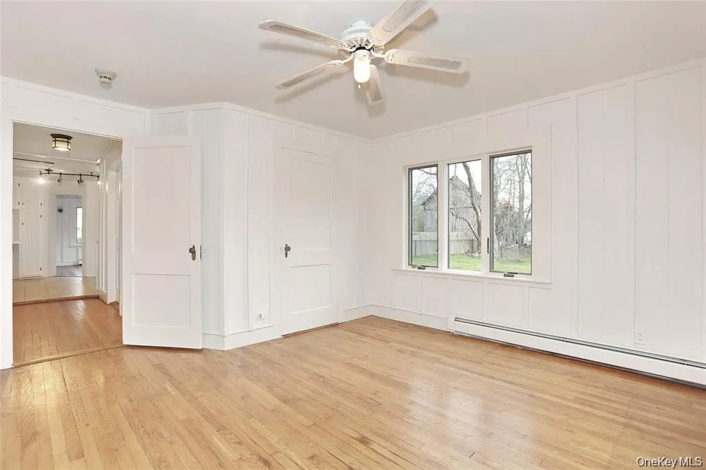 Empty room with a baseboard heating unit, light wood finished floors, a ceiling fan, and a decorative wall Empty room with a baseboard heating unit, light wood finished floors, a ceiling fan, and a decorative wall