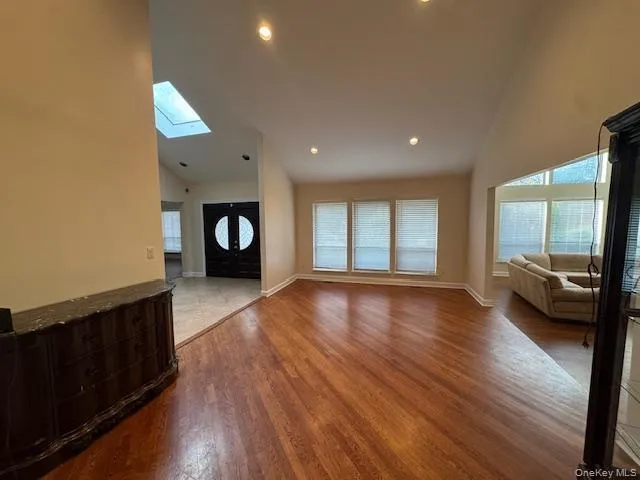 Unfurnished living room featuring high vaulted ceiling, light wood-style flooring, a skylight, and recessed lighting Unfurnished living room featuring high vaulted ceiling, light wood-style flooring, a skylight, and recessed lighting