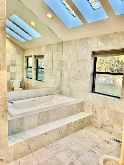 Full bathroom featuring tile walls, vaulted ceiling, a skylight, a bath, and recessed lighting Full bathroom featuring tile walls, vaulted ceiling, a skylight, a bath, and recessed lighting