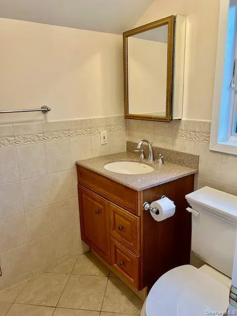 Half bathroom featuring vanity, wainscoting, tile walls, and light tile patterned floors Half bathroom featuring vanity, wainscoting, tile walls, and light tile patterned floors