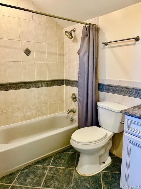 Full bathroom with tile walls, vanity, shower / bathtub combination with curtain, dark tile patterned floors, and a wainscoted wall Full bathroom with tile walls, vanity, shower / bathtub combination with curtain, dark tile patterned floors, and a wainscoted wall