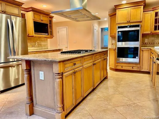 Kitchen with glass insert cabinets, backsplash, appliances with stainless steel finishes, a center island, and island range hood Kitchen with glass insert cabinets, backsplash, appliances with stainless steel finishes, a center island, and island range hood