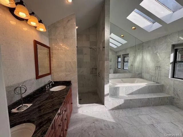 Full bath featuring tile walls, double vanity, a marble finish shower, lofted ceiling, and a garden tub Full bath featuring tile walls, double vanity, a marble finish shower, lofted ceiling, and a garden tub