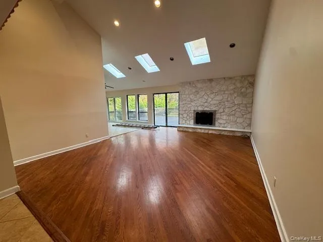 Unfurnished living room featuring light wood-style flooring, high vaulted ceiling, and a stone fireplace Unfurnished living room featuring light wood-style flooring, high vaulted ceiling, and a stone fireplace