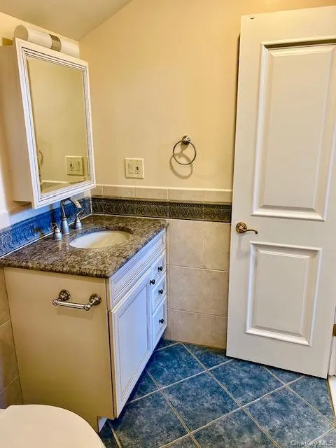 Half bathroom featuring tile walls, vanity, a wainscoted wall, and dark tile patterned flooring Half bathroom featuring tile walls, vanity, a wainscoted wall, and dark tile patterned flooring