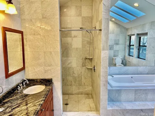 Bathroom with tile walls, a bath, vanity, a walk in shower, and a skylight Bathroom with tile walls, a bath, vanity, a walk in shower, and a skylight