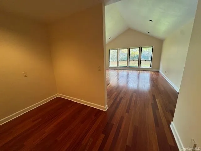 Empty room with dark wood-style flooring and vaulted ceiling Empty room with dark wood-style flooring and vaulted ceiling