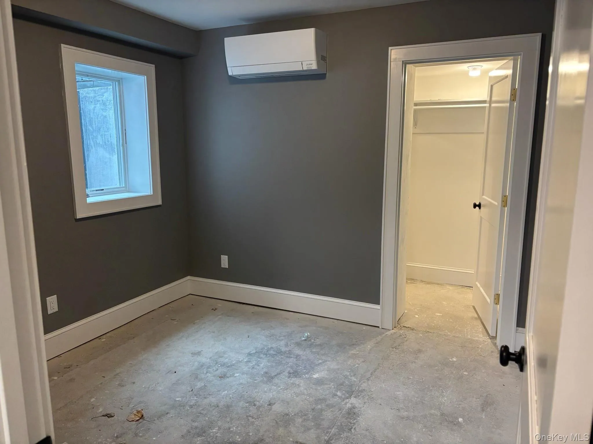 Unfurnished bedroom featuring a wall unit AC, unfinished concrete flooring, and a spacious closet Unfurnished bedroom featuring a wall unit AC, unfinished concrete flooring, and a spacious closet