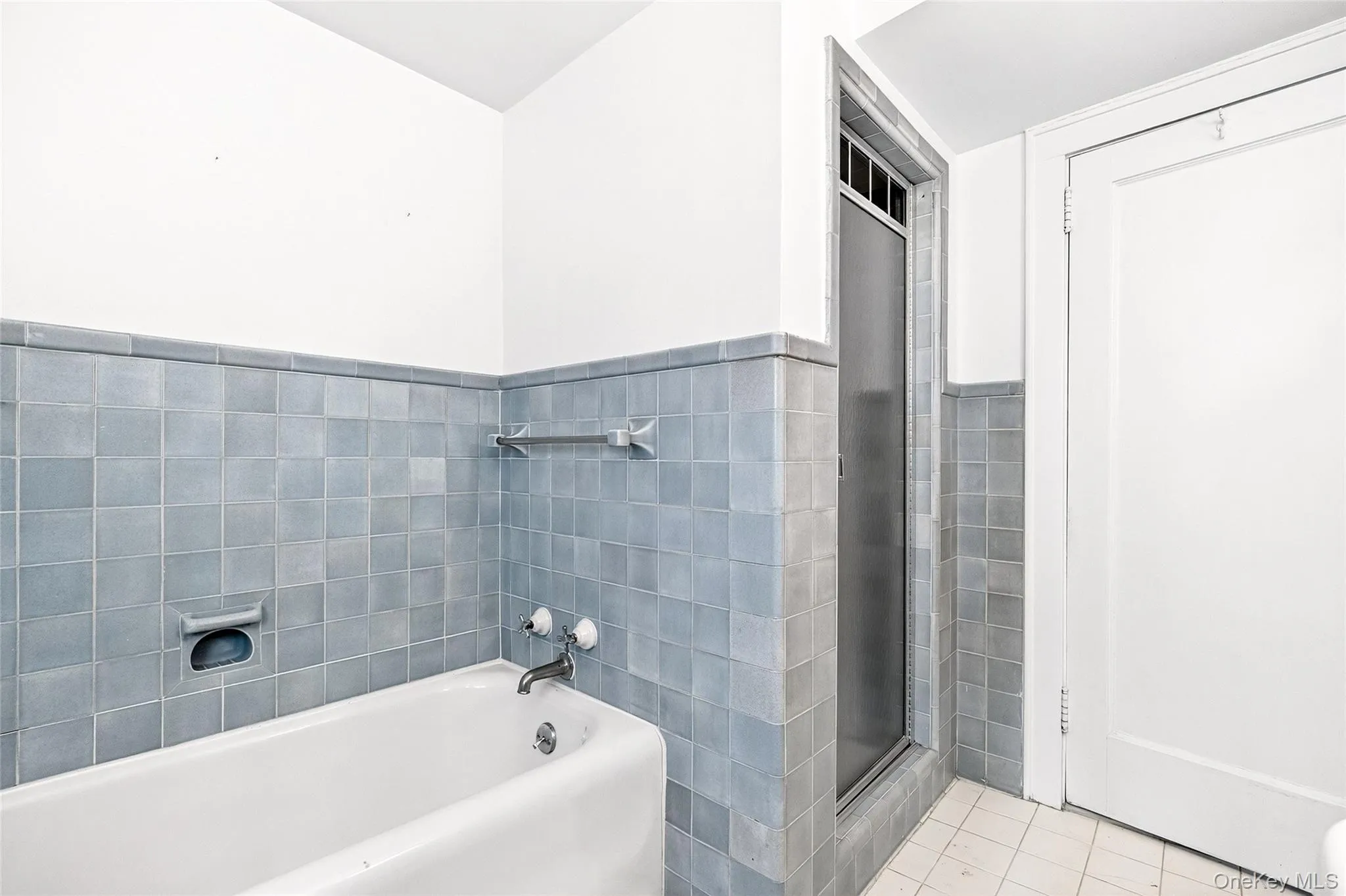 Full bath with a garden tub, a stall shower, tile walls, light tile patterned flooring, and a wainscoted wall Full bath with a garden tub, a stall shower, tile walls, light tile patterned flooring, and a wainscoted wall
