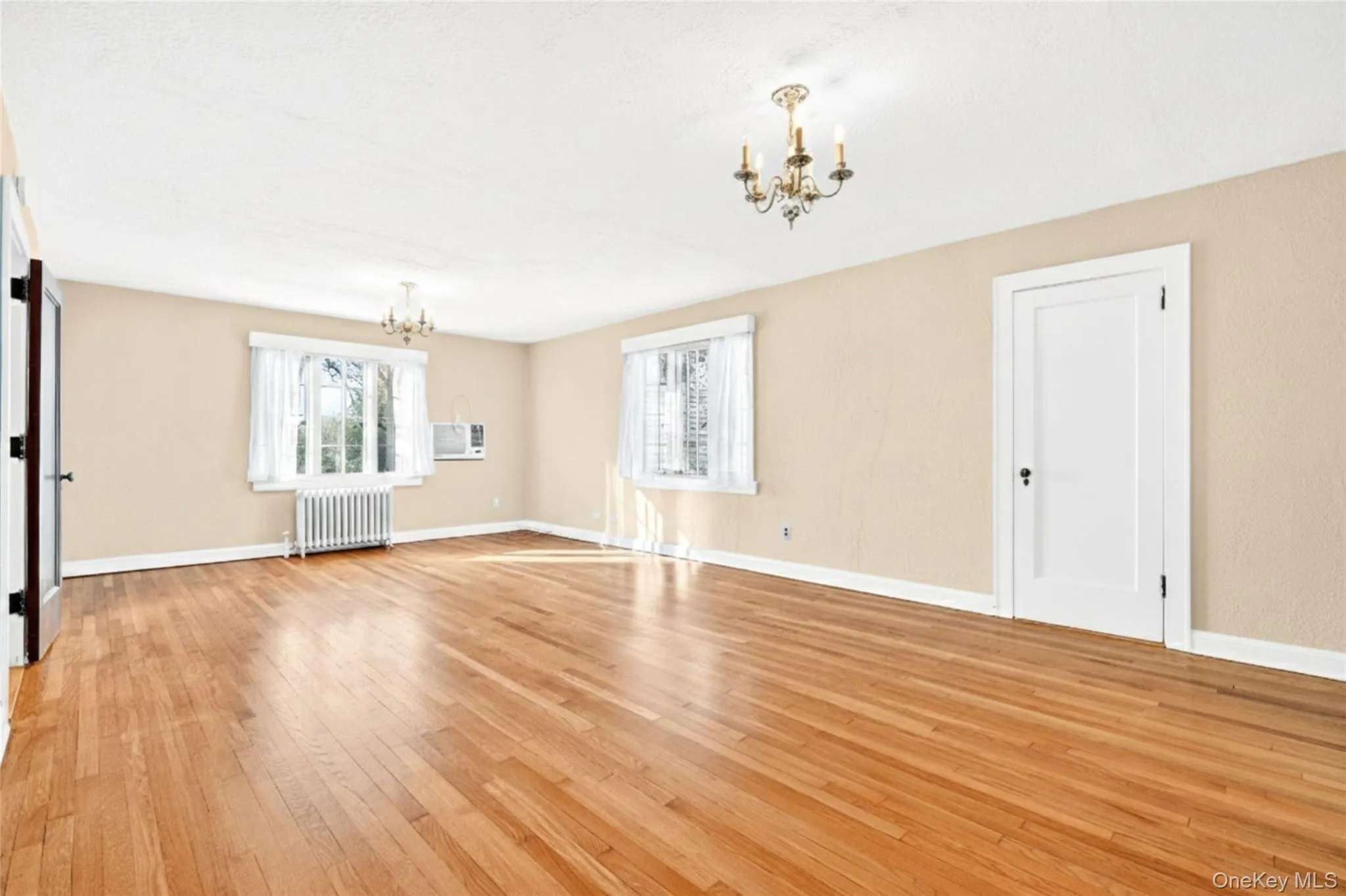 Unfurnished living room featuring a chandelier, light wood-style floors, and radiator heating unit Unfurnished living room featuring a chandelier, light wood-style floors, and radiator heating unit