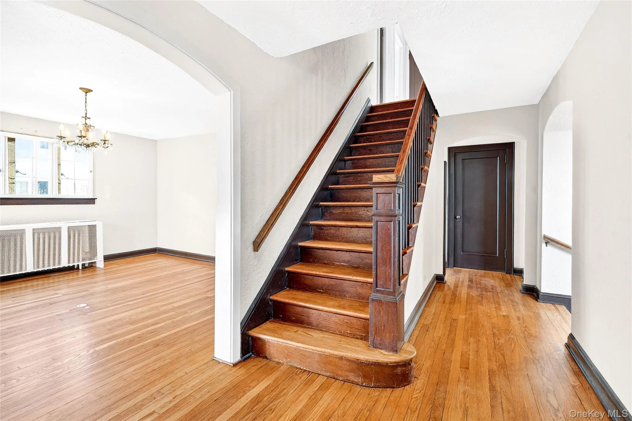 Stairway with arched walkways, radiator heating unit, hardwood / wood-style floors, and a chandelier Stairway with arched walkways, radiator heating unit, hardwood / wood-style floors, and a chandelier