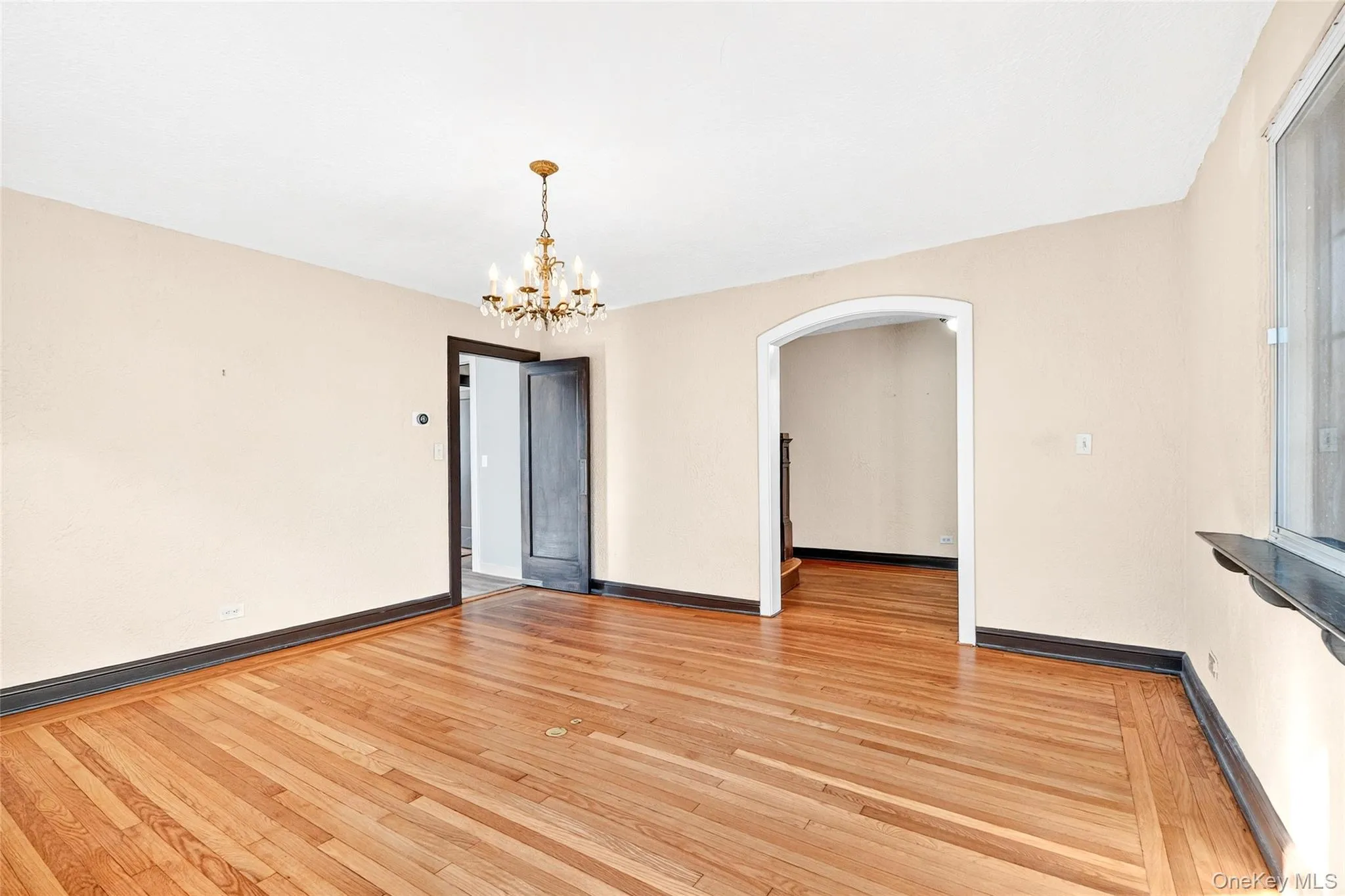 Unfurnished room with arched walkways, light wood-type flooring, and a chandelier Unfurnished room with arched walkways, light wood-type flooring, and a chandelier