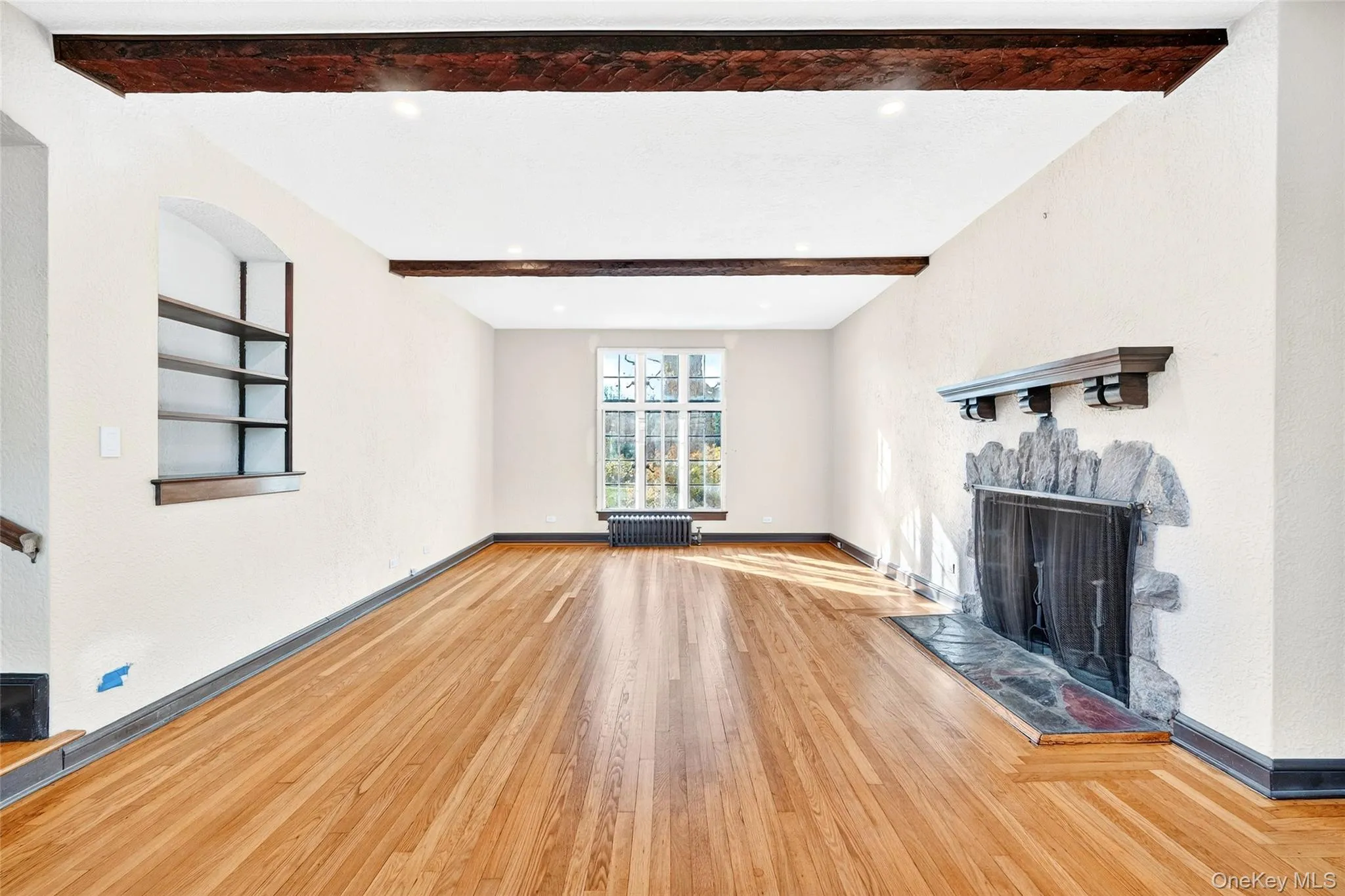 Unfurnished living room with a fireplace with raised hearth, beamed ceiling, wood-type flooring, and radiator Unfurnished living room with a fireplace with raised hearth, beamed ceiling, wood-type flooring, and radiator