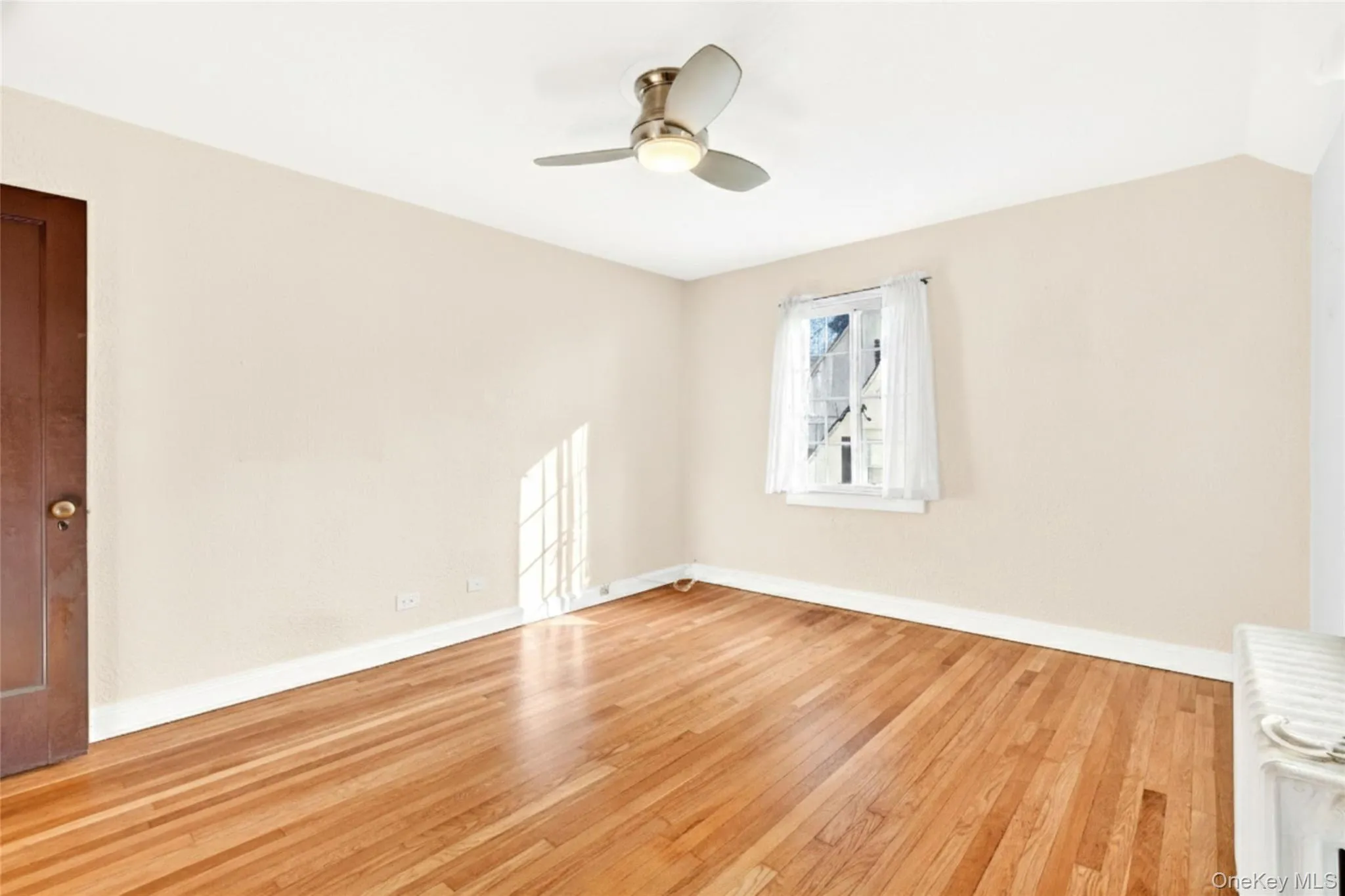 Empty room featuring light wood-type flooring, a ceiling fan, and radiator heating unit Empty room featuring light wood-type flooring, a ceiling fan, and radiator heating unit