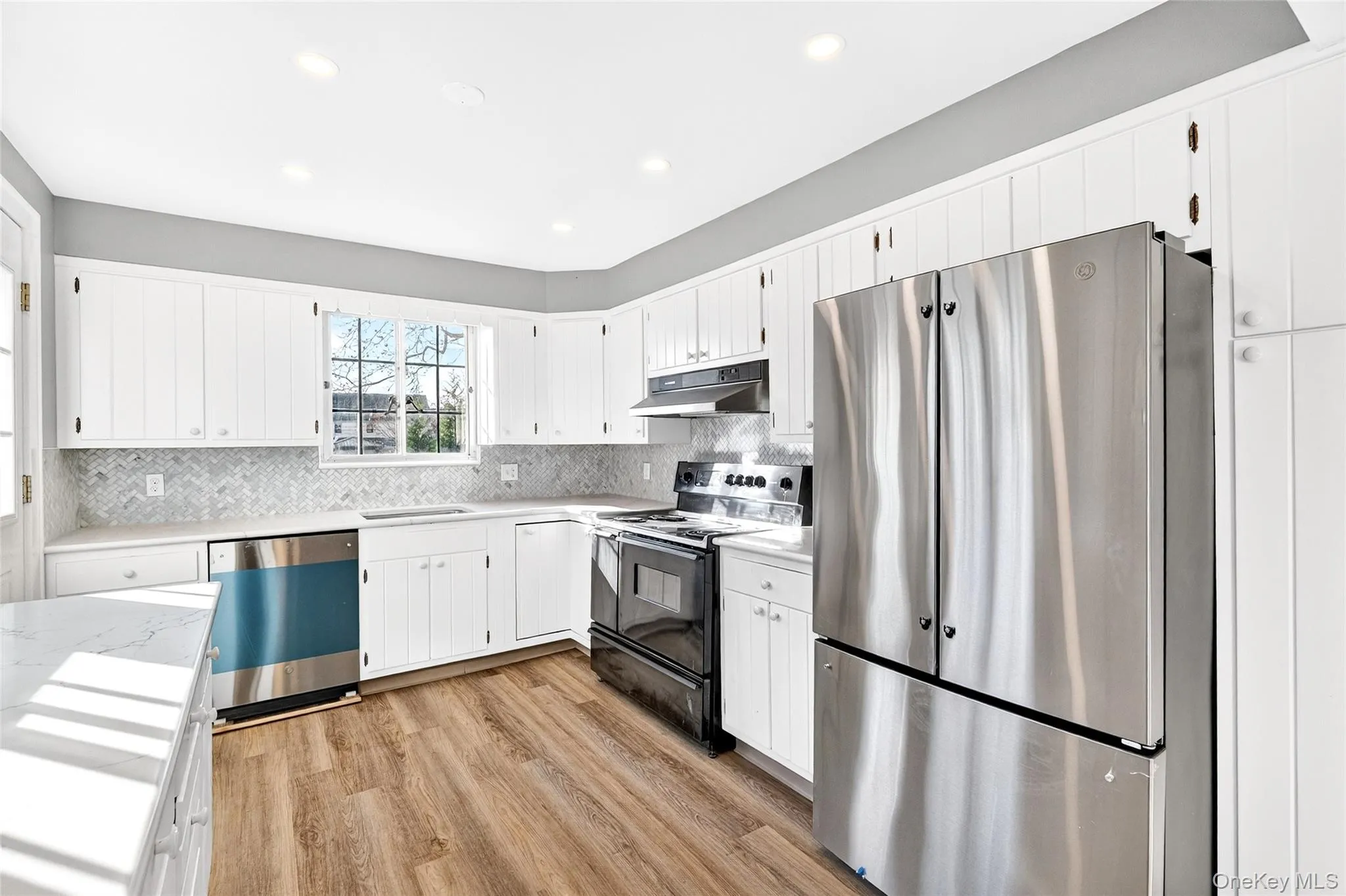 Kitchen with stainless steel appliances, white cabinetry, under cabinet range hood, light wood-style flooring, and backsplash Kitchen with stainless steel appliances, white cabinetry, under cabinet range hood, light wood-style flooring, and backsplash