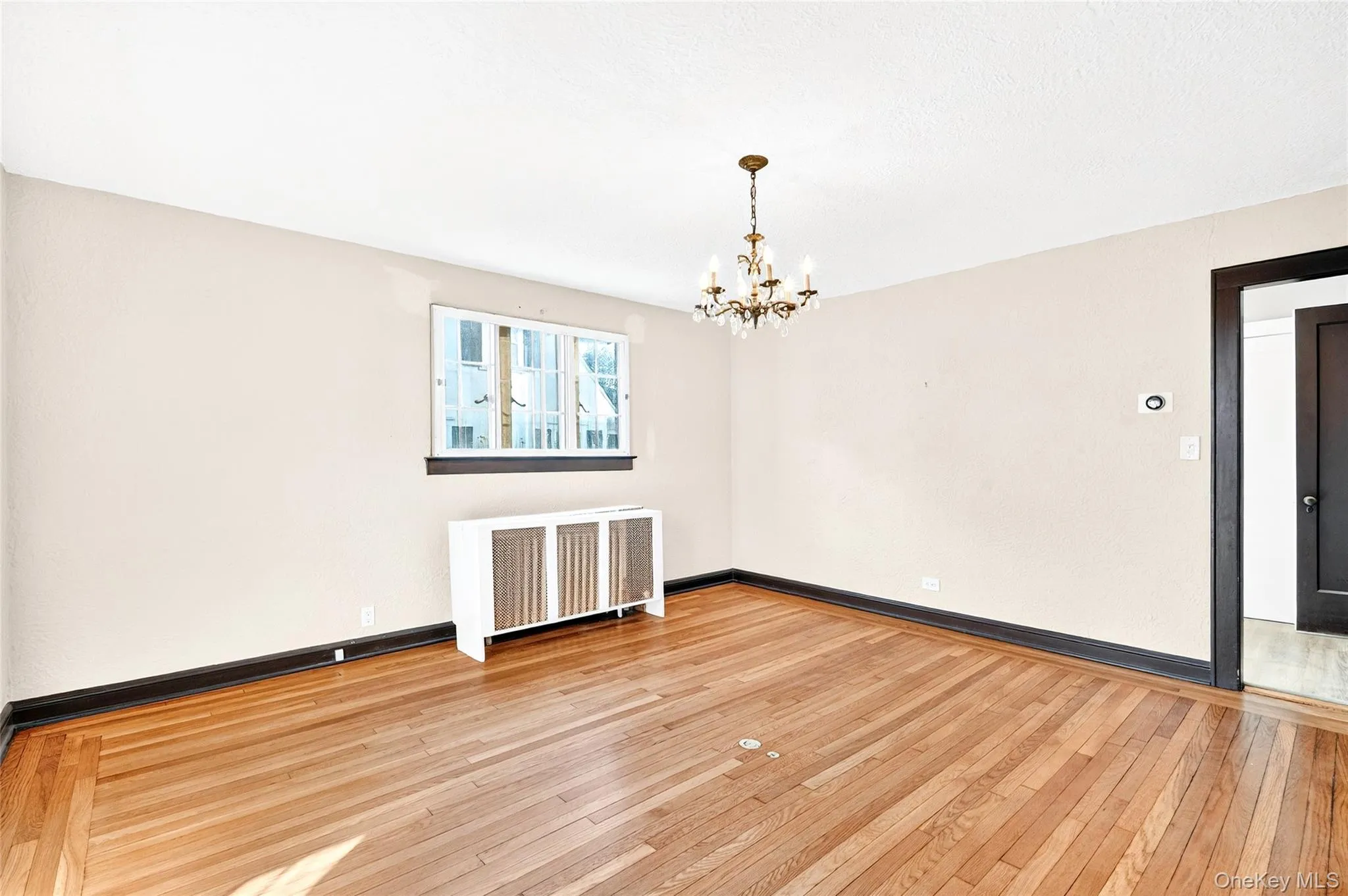 Unfurnished room featuring radiator heating unit, light wood-style floors, and a chandelier Unfurnished room featuring radiator heating unit, light wood-style floors, and a chandelier