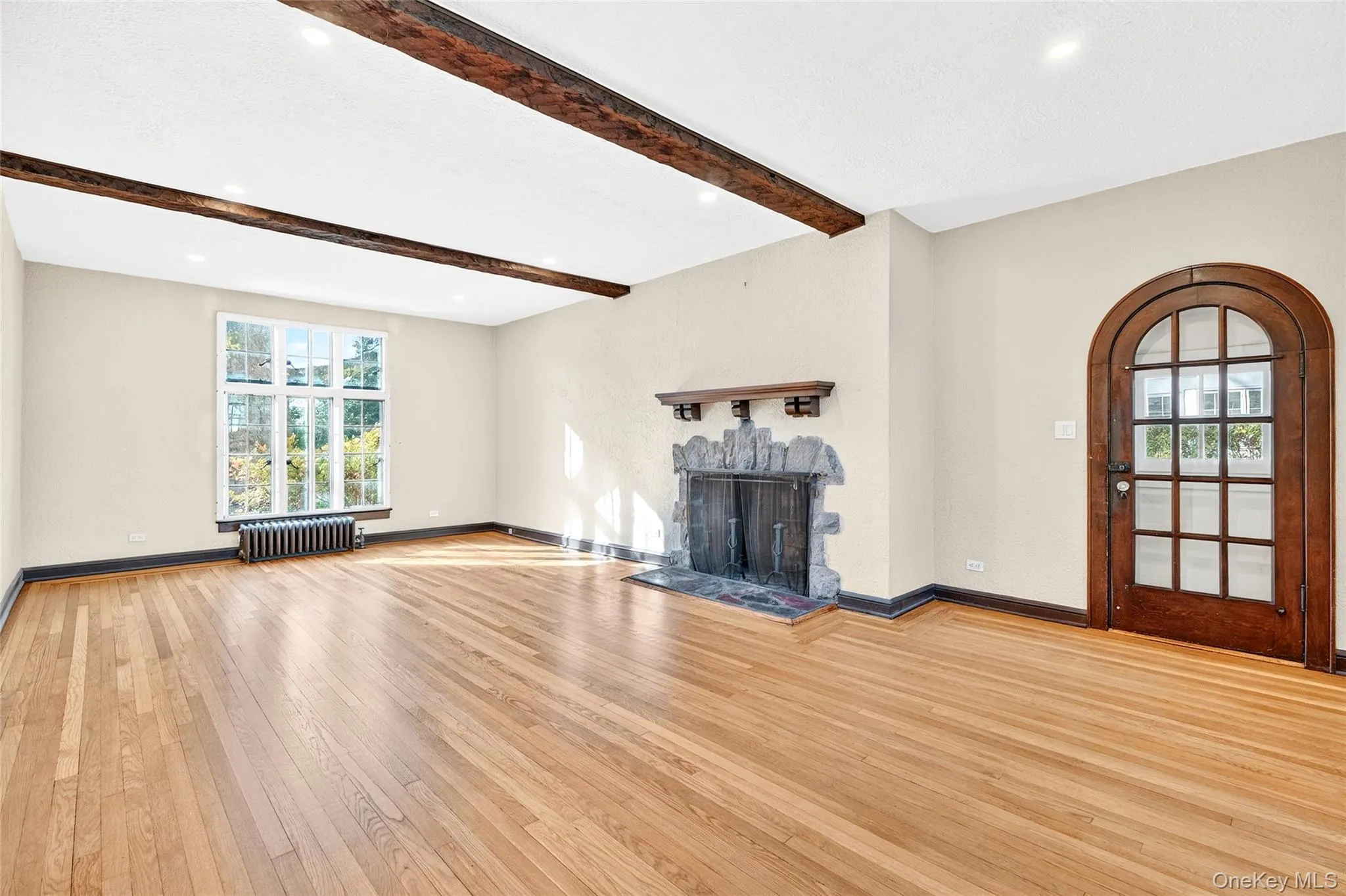 Unfurnished living room with a fireplace with raised hearth, hardwood / wood-style floors, radiator heating unit, beam ceiling, and recessed lighting Unfurnished living room with a fireplace with raised hearth, hardwood / wood-style floors, radiator heating unit, beam ceiling, and recessed lighting