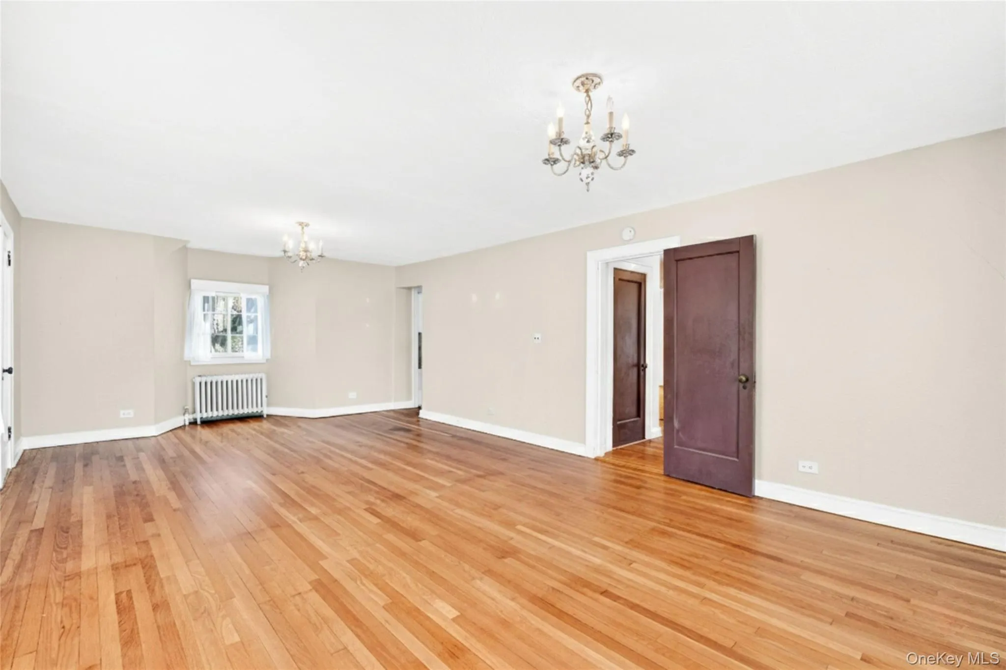 Spare room featuring a chandelier, radiator heating unit, and light wood-style floors Spare room featuring a chandelier, radiator heating unit, and light wood-style floors