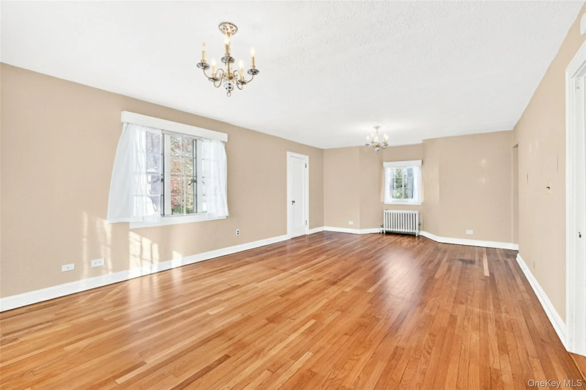 Unfurnished living room featuring a chandelier, light wood-style floors, radiator, and a textured ceiling Unfurnished living room featuring a chandelier, light wood-style floors, radiator, and a textured ceiling