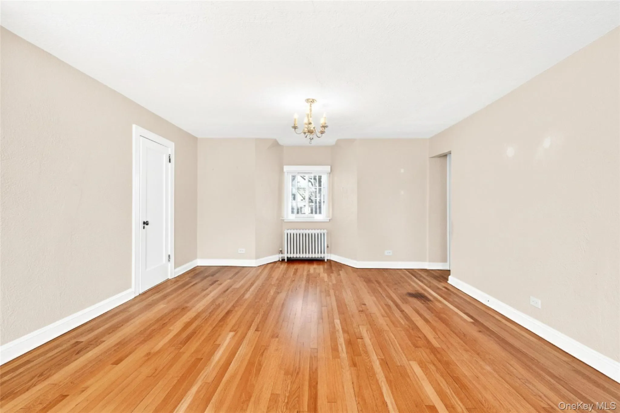 Empty room with a chandelier, radiator heating unit, and light wood-type flooring Empty room with a chandelier, radiator heating unit, and light wood-type flooring