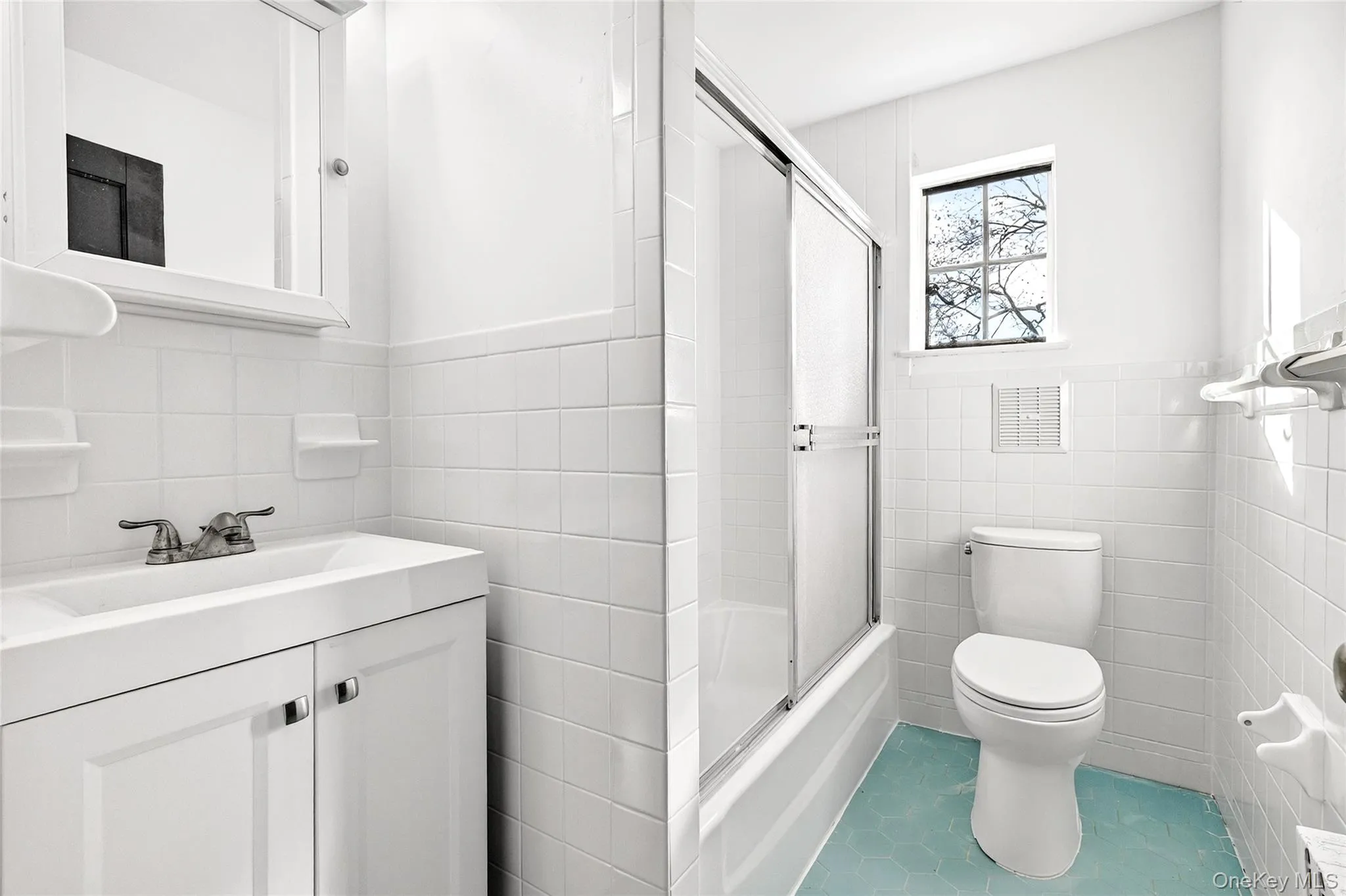 Full bathroom with tile walls, a wainscoted wall, vanity, shower / bath combination with glass door, and tile patterned flooring Full bathroom with tile walls, a wainscoted wall, vanity, shower / bath combination with glass door, and tile patterned flooring