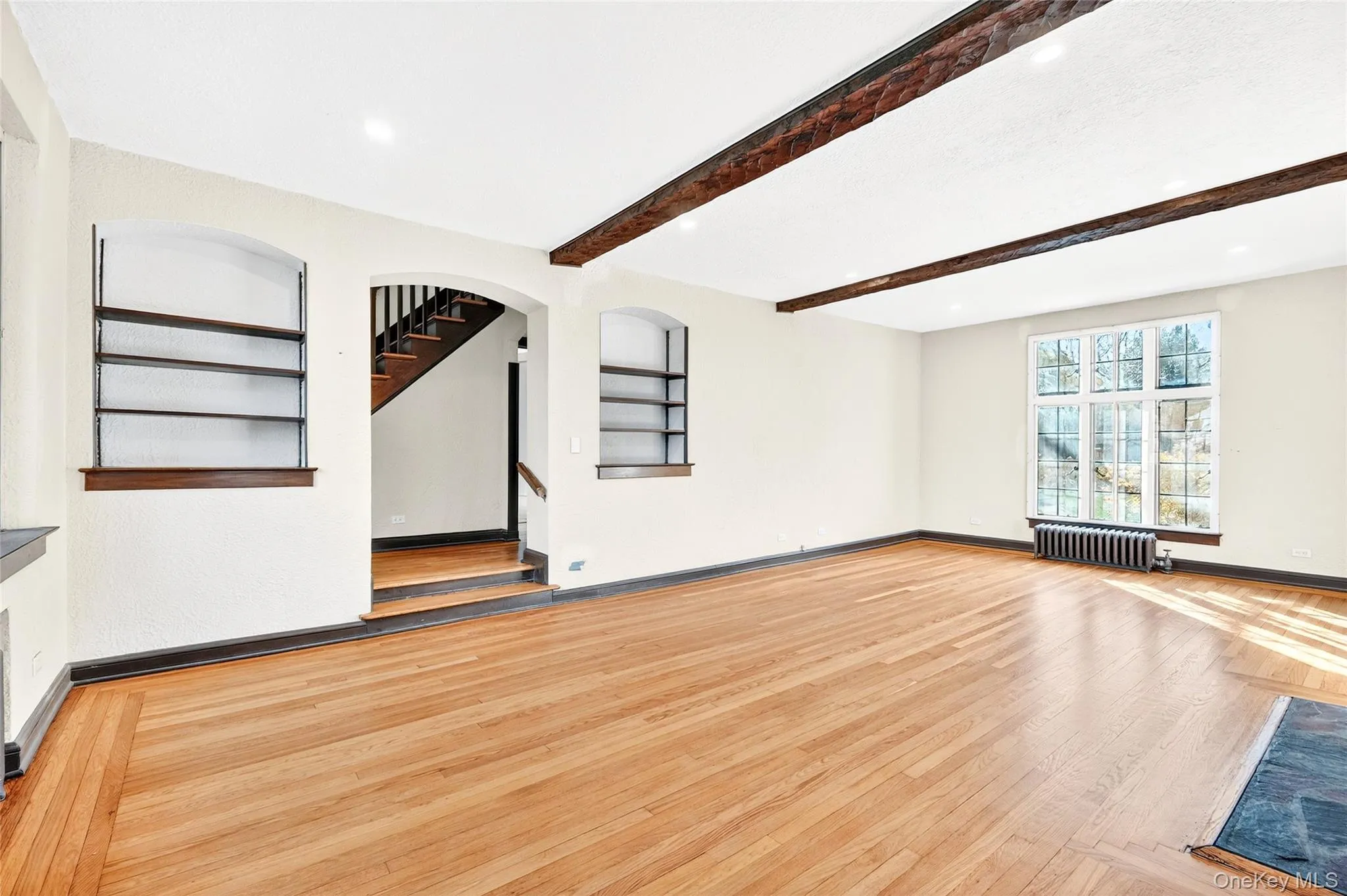 Unfurnished living room with light wood-style floors, recessed lighting, radiator heating unit, and beamed ceiling Unfurnished living room with light wood-style floors, recessed lighting, radiator heating unit, and beamed ceiling