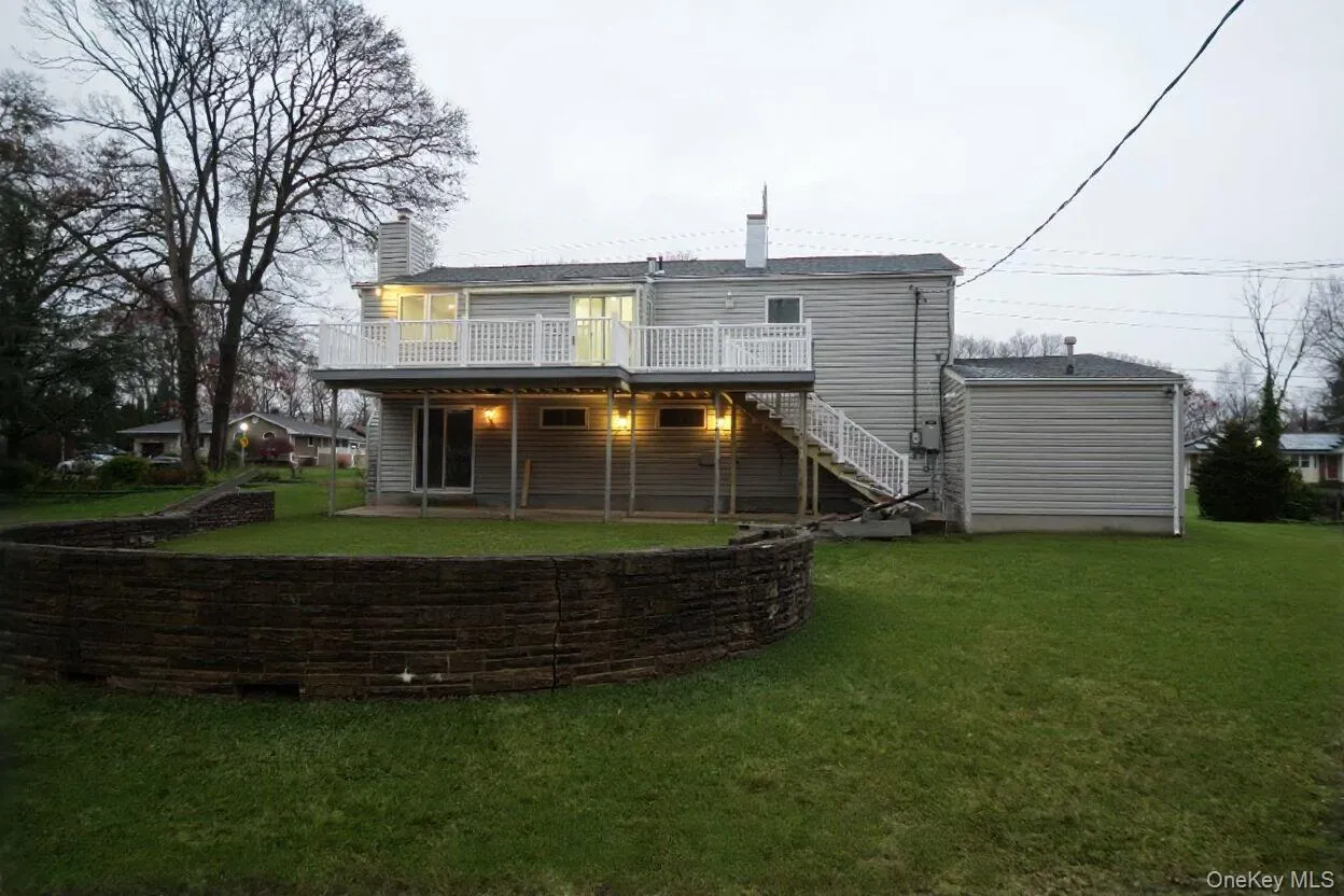 Rear view of house with stairway, a chimney, a wooden deck, and a lawn Rear view of house with stairway, a chimney, a wooden deck, and a lawn