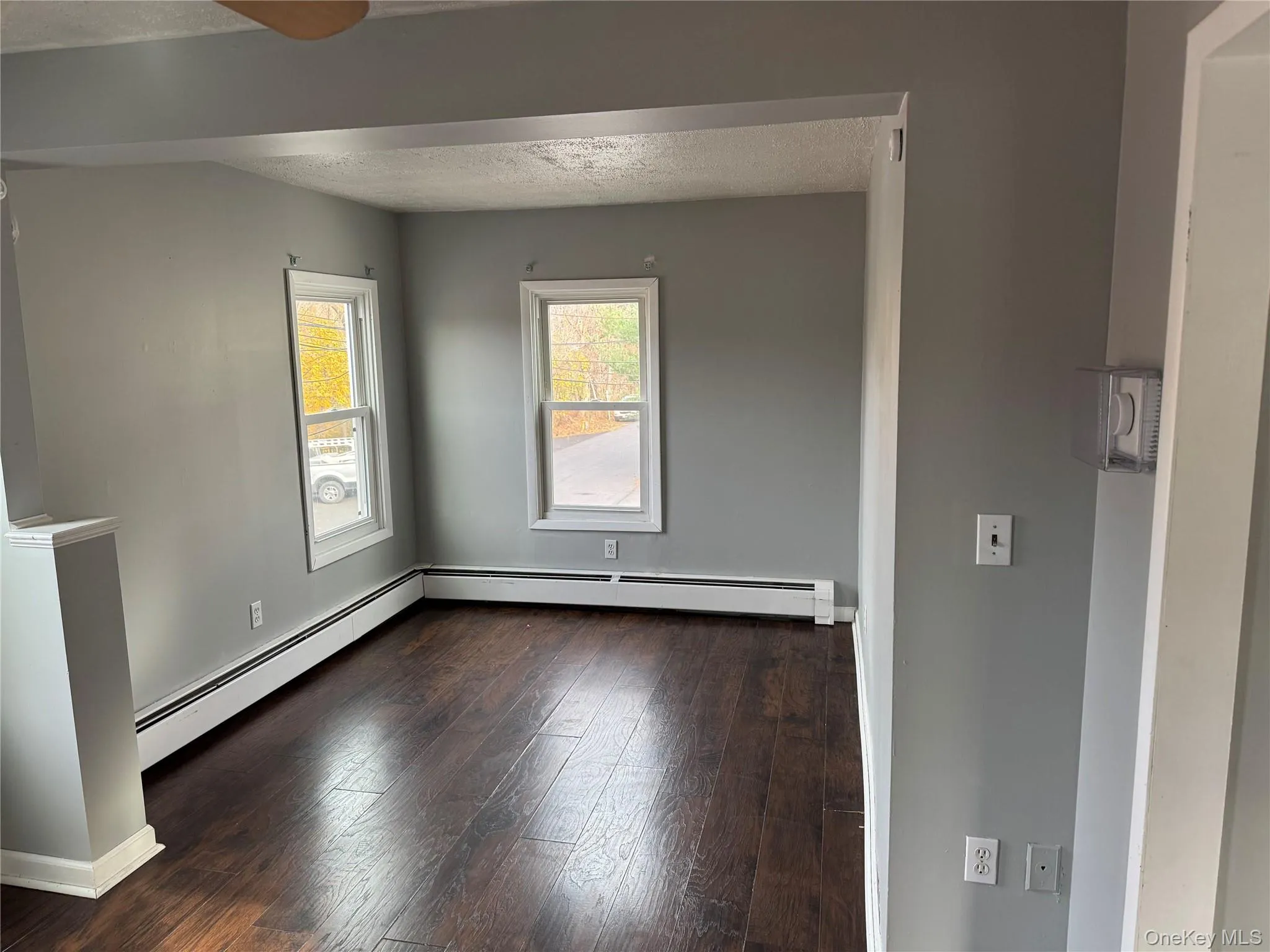 Empty room featuring a baseboard heating unit, dark wood-style floors, and a textured ceiling Empty room featuring a baseboard heating unit, dark wood-style floors, and a textured ceiling