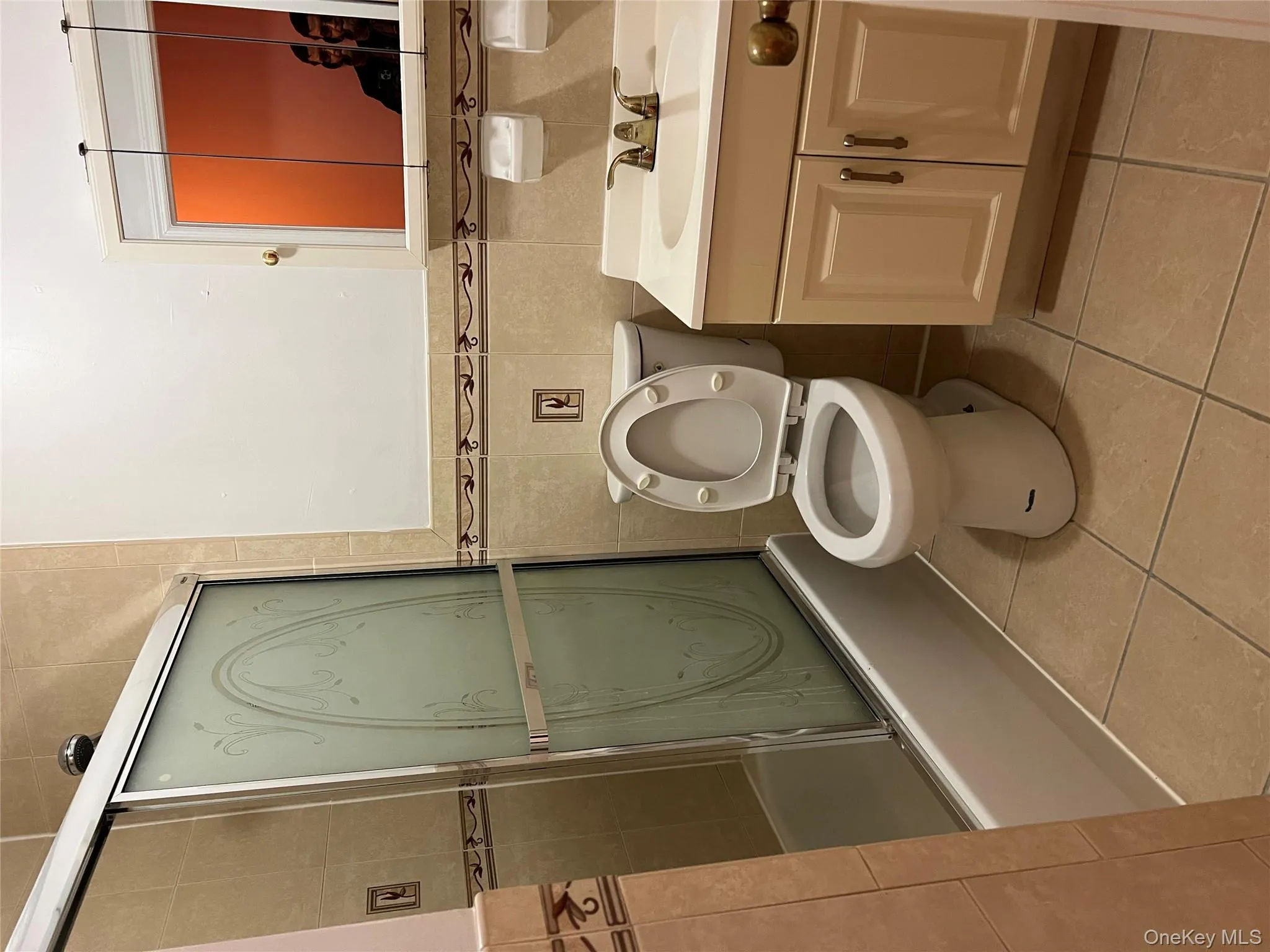 Full bathroom featuring vanity, light tile patterned floors, bath / shower combo with glass door, tile walls, and wainscoting Full bathroom featuring vanity, light tile patterned floors, bath / shower combo with glass door, tile walls, and wainscoting