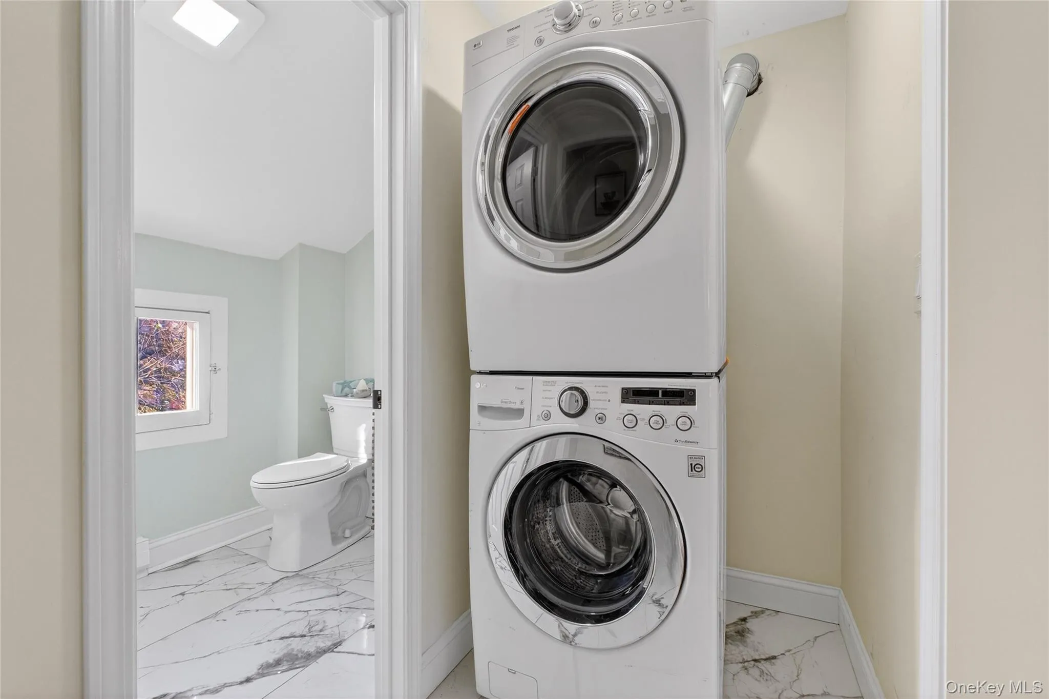 Laundry area with light marble finish flooring and stacked washer / dryer Laundry area with light marble finish flooring and stacked washer / dryer