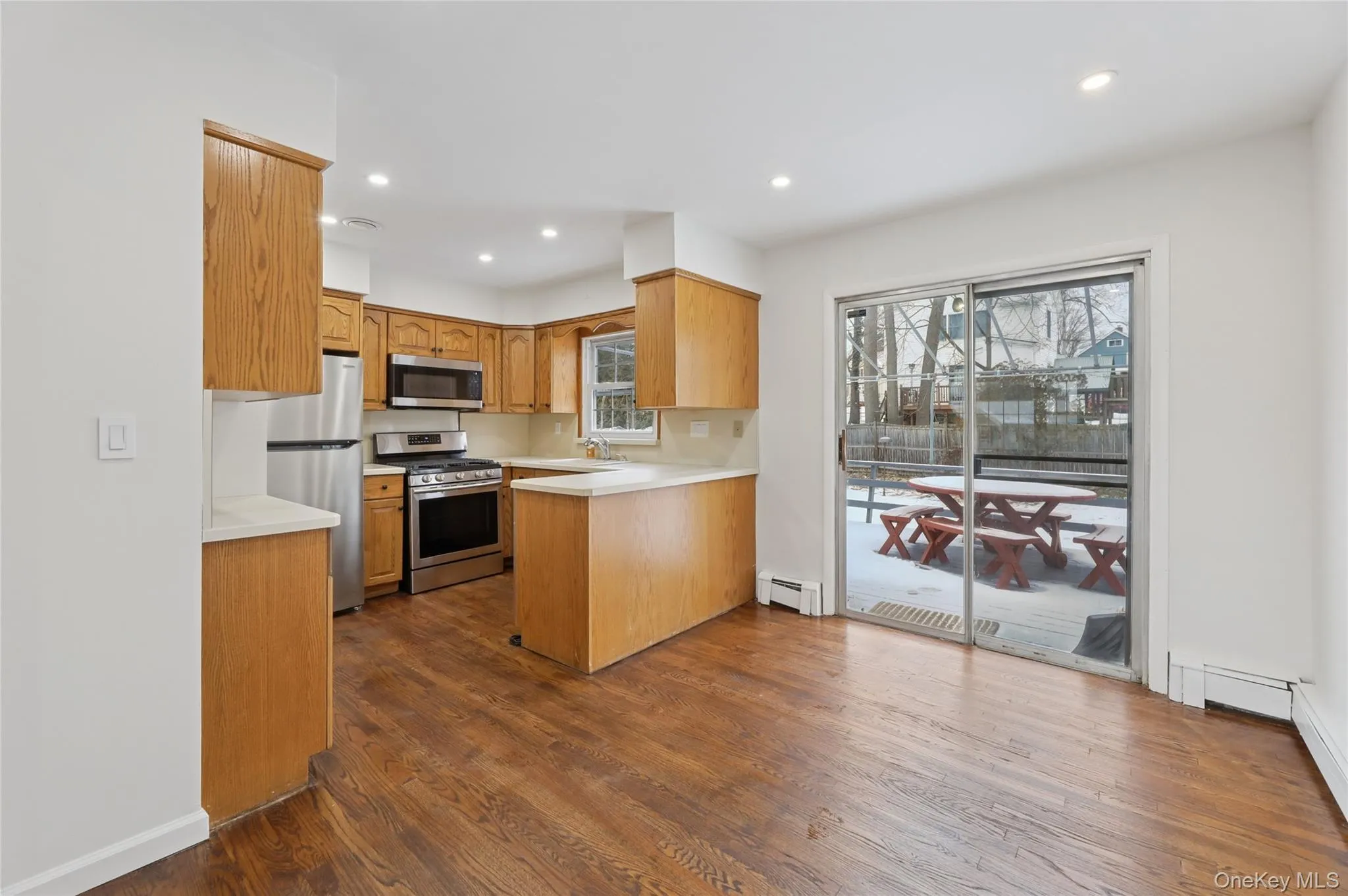 Kitchen with light countertops, appliances with stainless steel finishes, recessed lighting, dark wood-style floors, and a peninsula Kitchen with light countertops, appliances with stainless steel finishes, recessed lighting, dark wood-style floors, and a peninsula