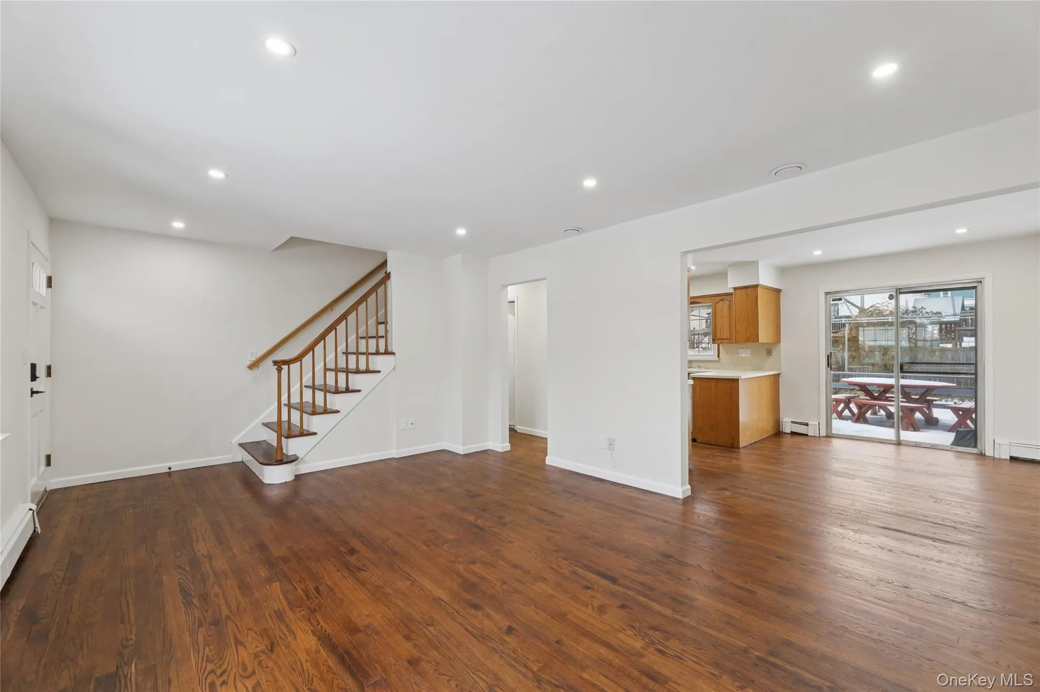 Unfurnished living room featuring stairs, dark wood-style flooring, recessed lighting, and a baseboard heating unit Unfurnished living room featuring stairs, dark wood-style flooring, recessed lighting, and a baseboard heating unit