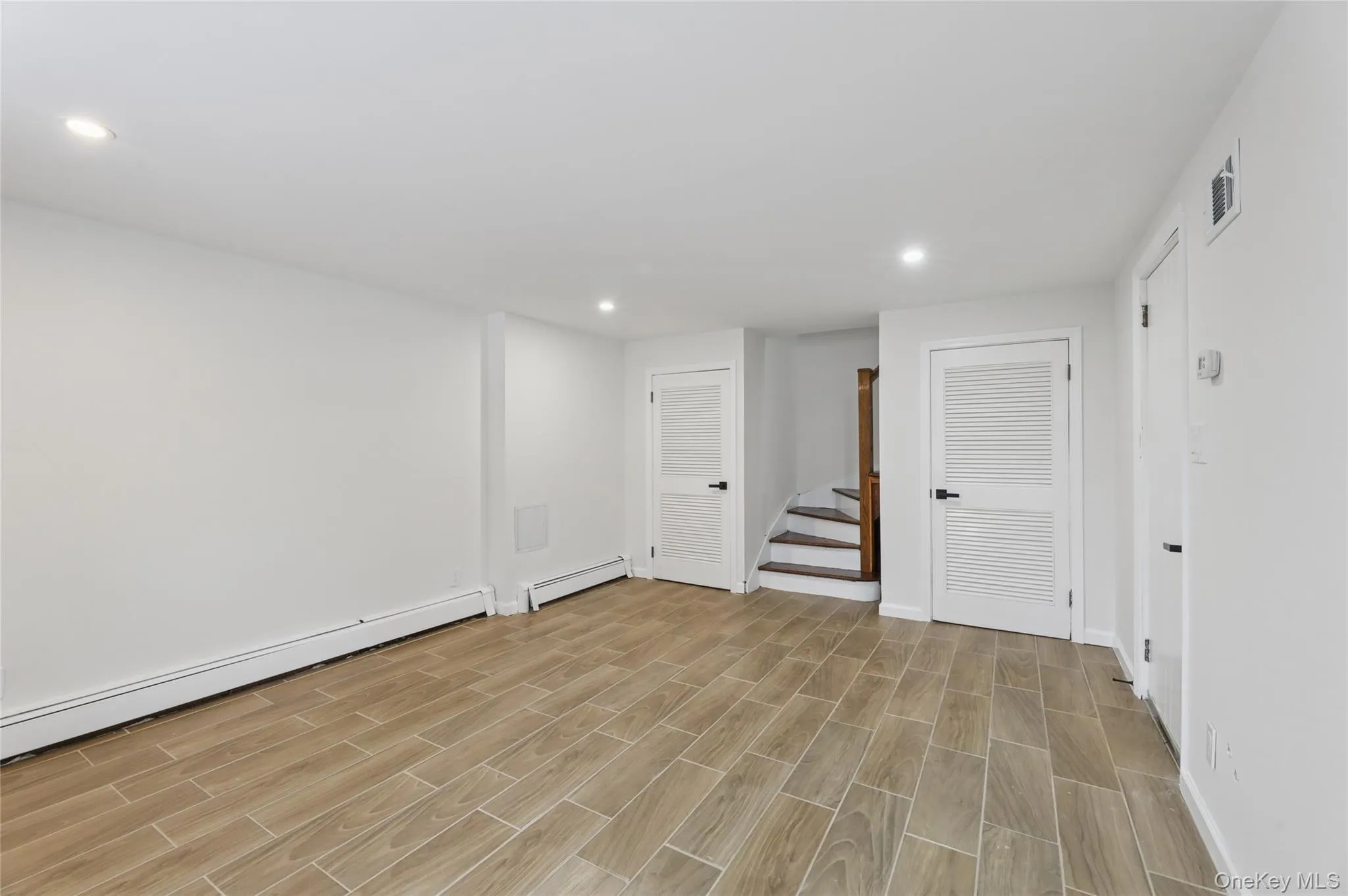 Basement featuring stairway, recessed lighting, wood finish floors, a baseboard radiator, and baseboard heating Basement featuring stairway, recessed lighting, wood finish floors, a baseboard radiator, and baseboard heating
