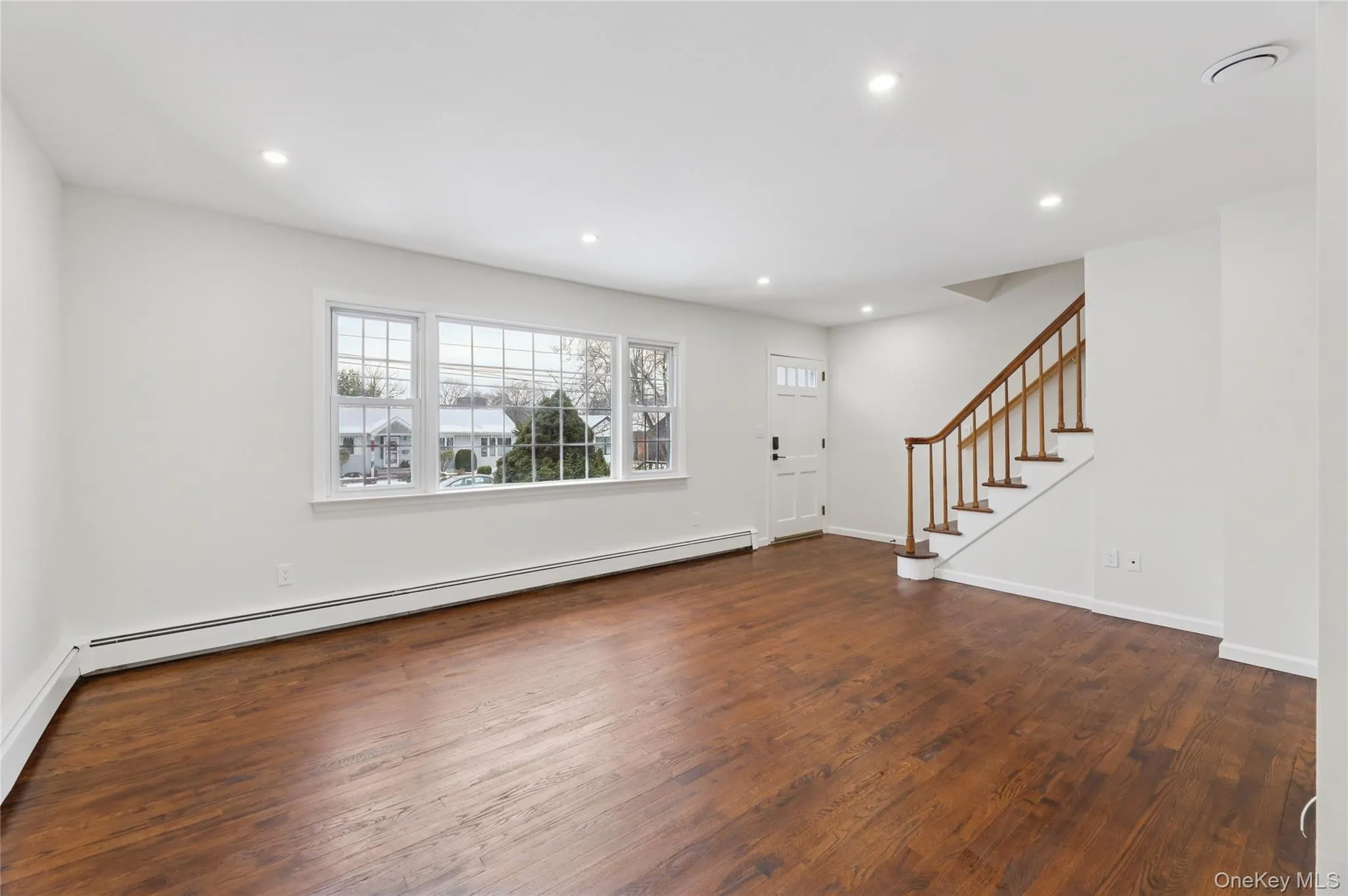Unfurnished living room with stairway, baseboard heating, dark wood-style floors, and recessed lighting Unfurnished living room with stairway, baseboard heating, dark wood-style floors, and recessed lighting