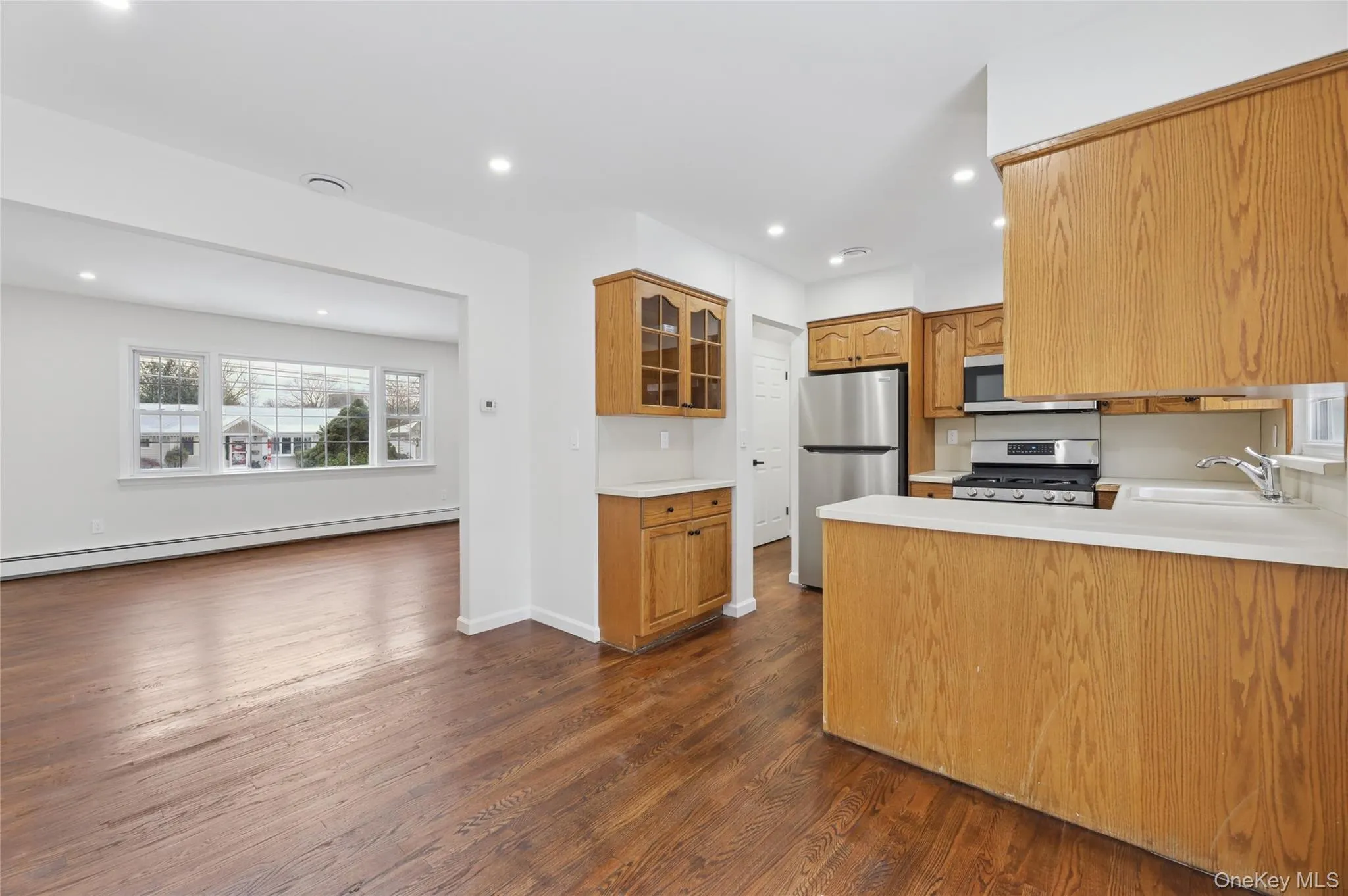 Kitchen featuring glass insert cabinets, light countertops, appliances with stainless steel finishes, a peninsula, and dark wood-type flooring Kitchen featuring glass insert cabinets, light countertops, appliances with stainless steel finishes, a peninsula, and dark wood-type flooring