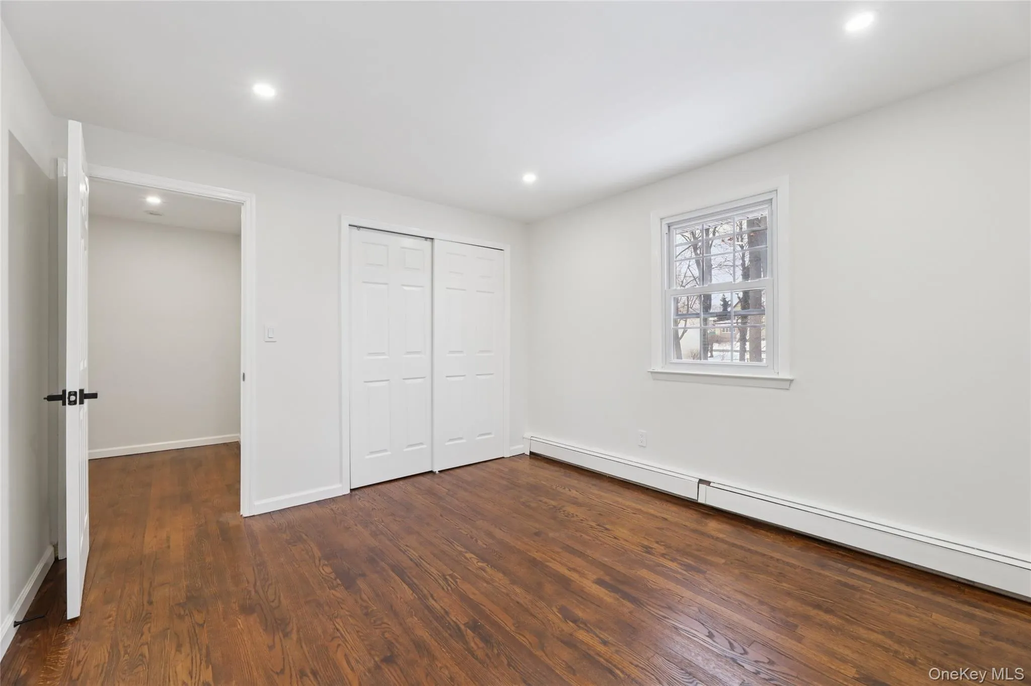 Unfurnished bedroom with a baseboard heating unit, dark wood finished floors, a closet, and recessed lighting Unfurnished bedroom with a baseboard heating unit, dark wood finished floors, a closet, and recessed lighting