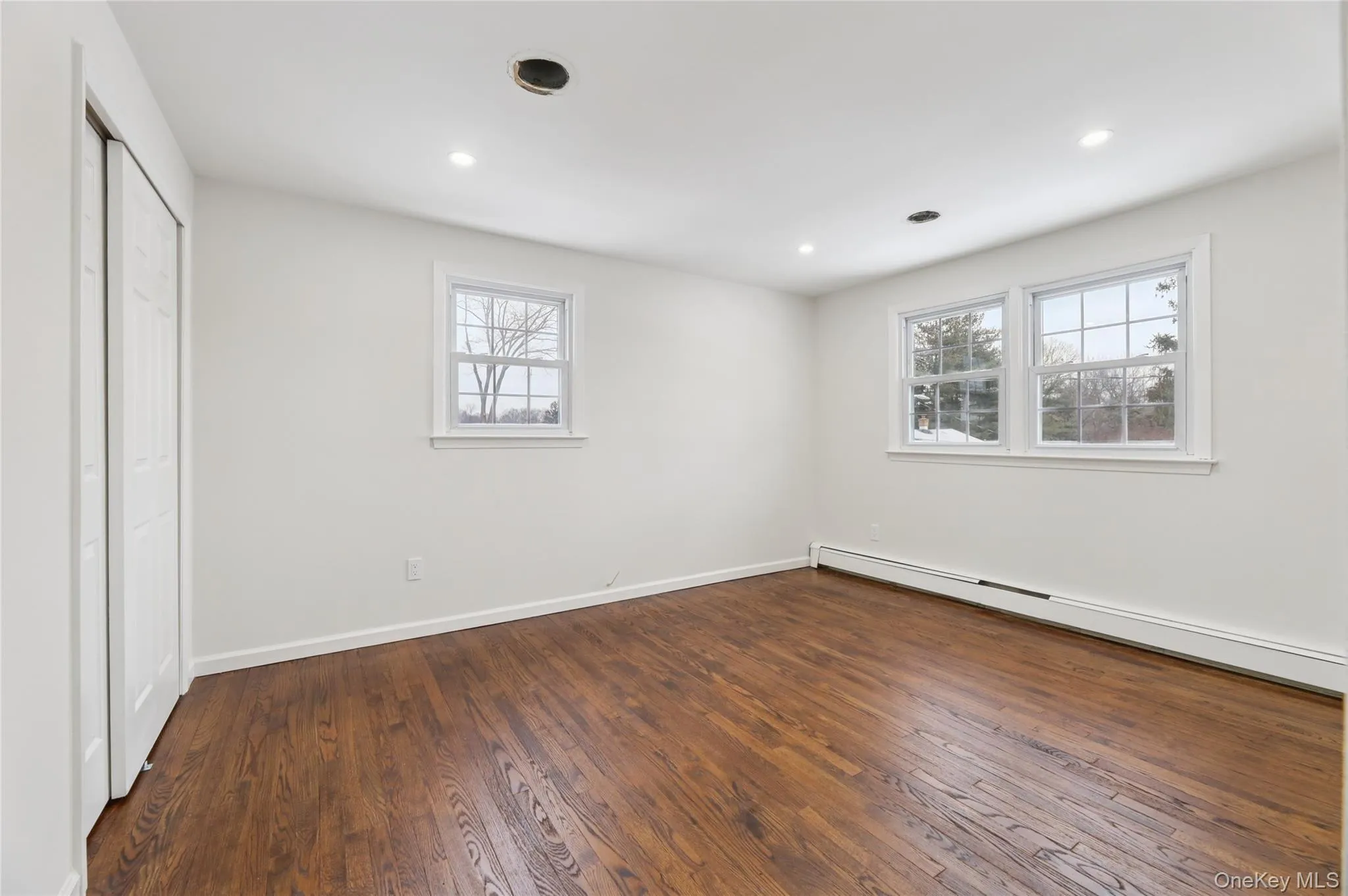 Unfurnished bedroom featuring a baseboard heating unit, dark wood-type flooring, multiple windows, and recessed lighting Unfurnished bedroom featuring a baseboard heating unit, dark wood-type flooring, multiple windows, and recessed lighting
