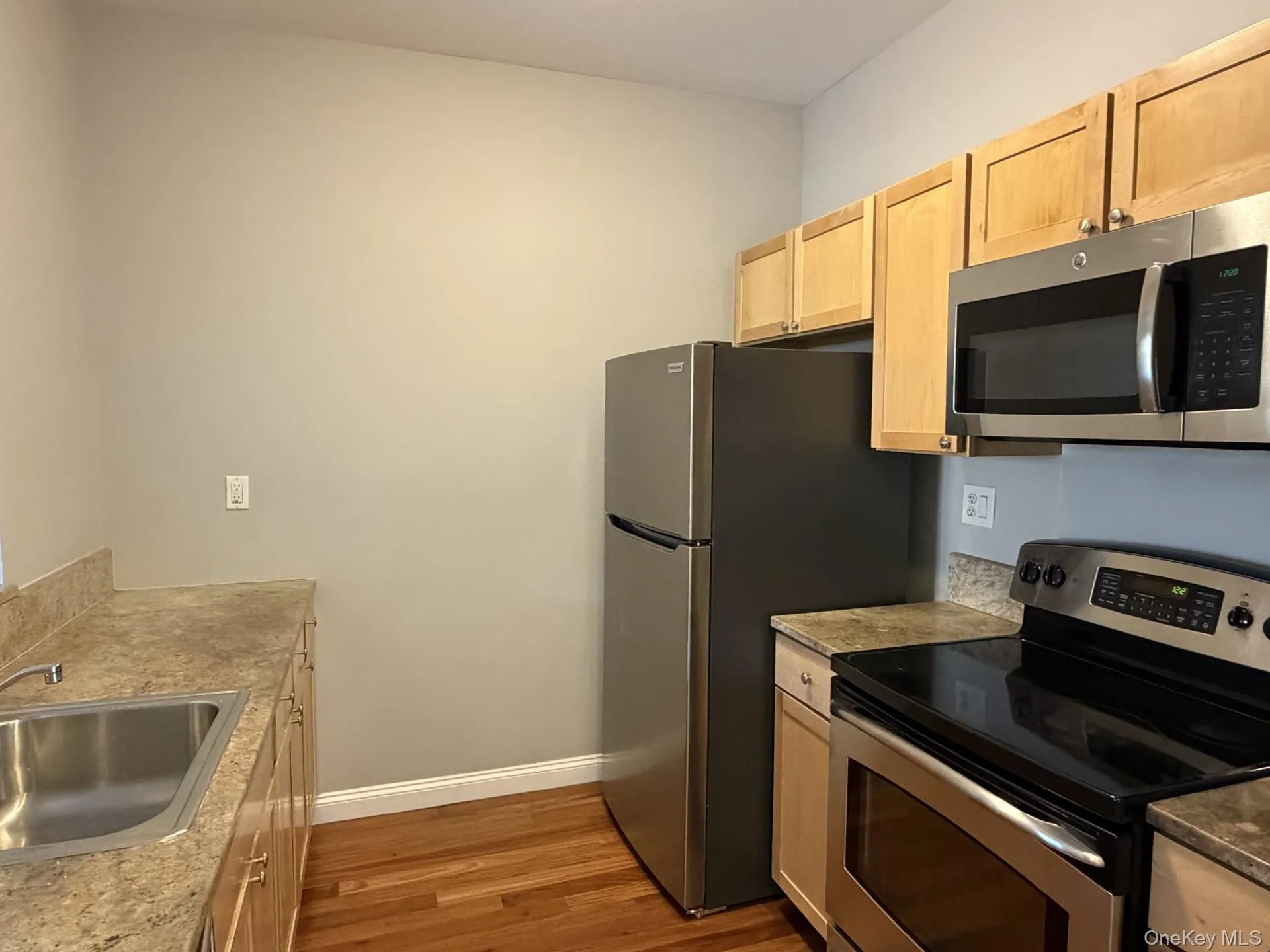 Kitchen with appliances with stainless steel finishes, light brown cabinets, dark wood-style flooring, and light countertops Kitchen with appliances with stainless steel finishes, light brown cabinets, dark wood-style flooring, and light countertops