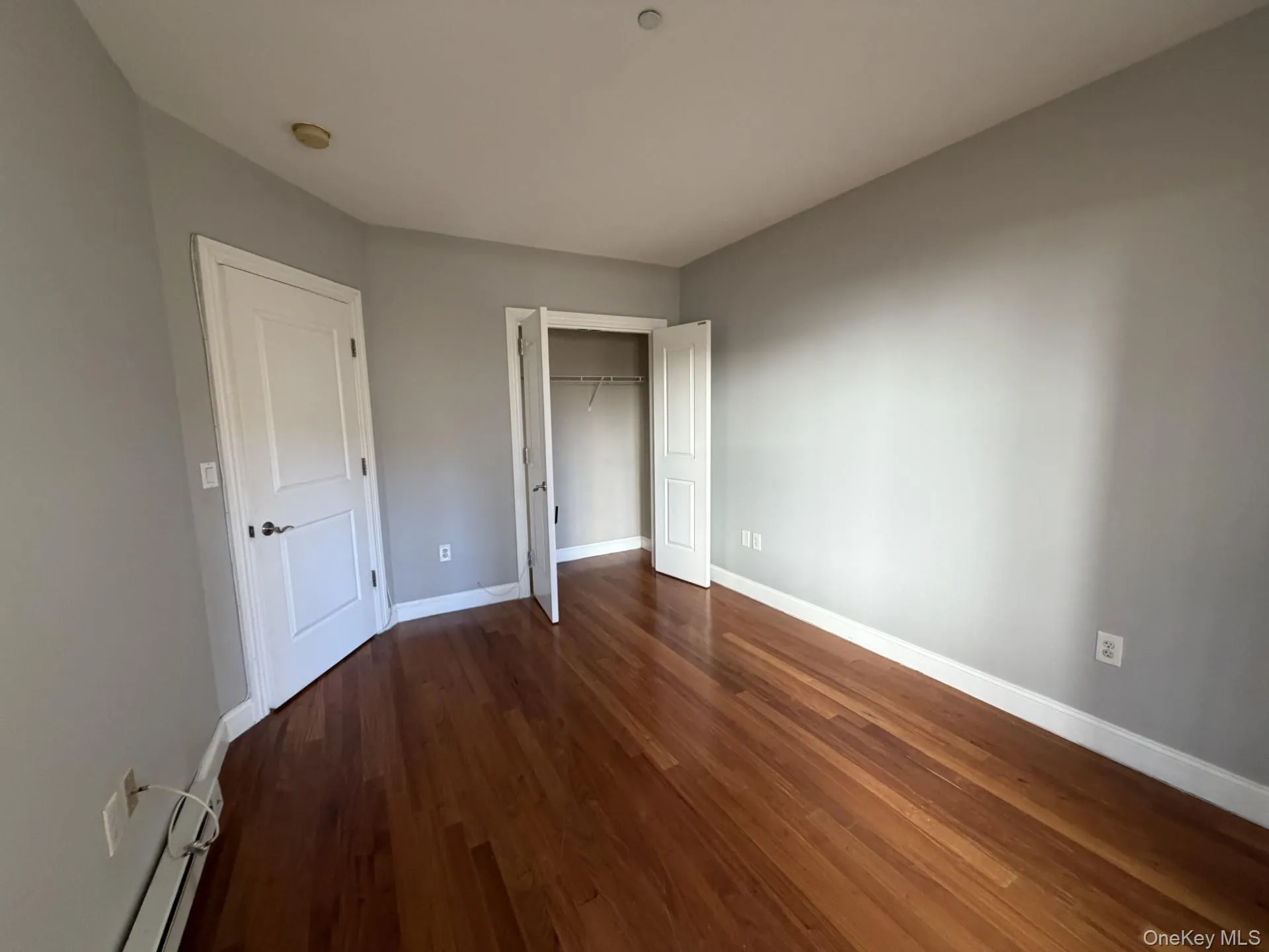 Unfurnished bedroom with dark wood finished floors, a closet, and baseboard heating Unfurnished bedroom with dark wood finished floors, a closet, and baseboard heating