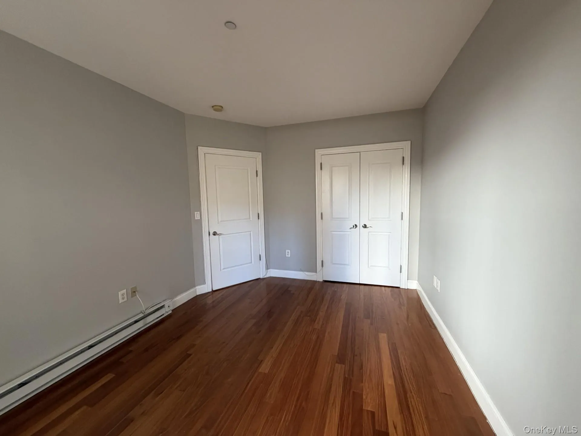 Unfurnished bedroom with a baseboard radiator, dark wood-type flooring, and a closet Unfurnished bedroom with a baseboard radiator, dark wood-type flooring, and a closet