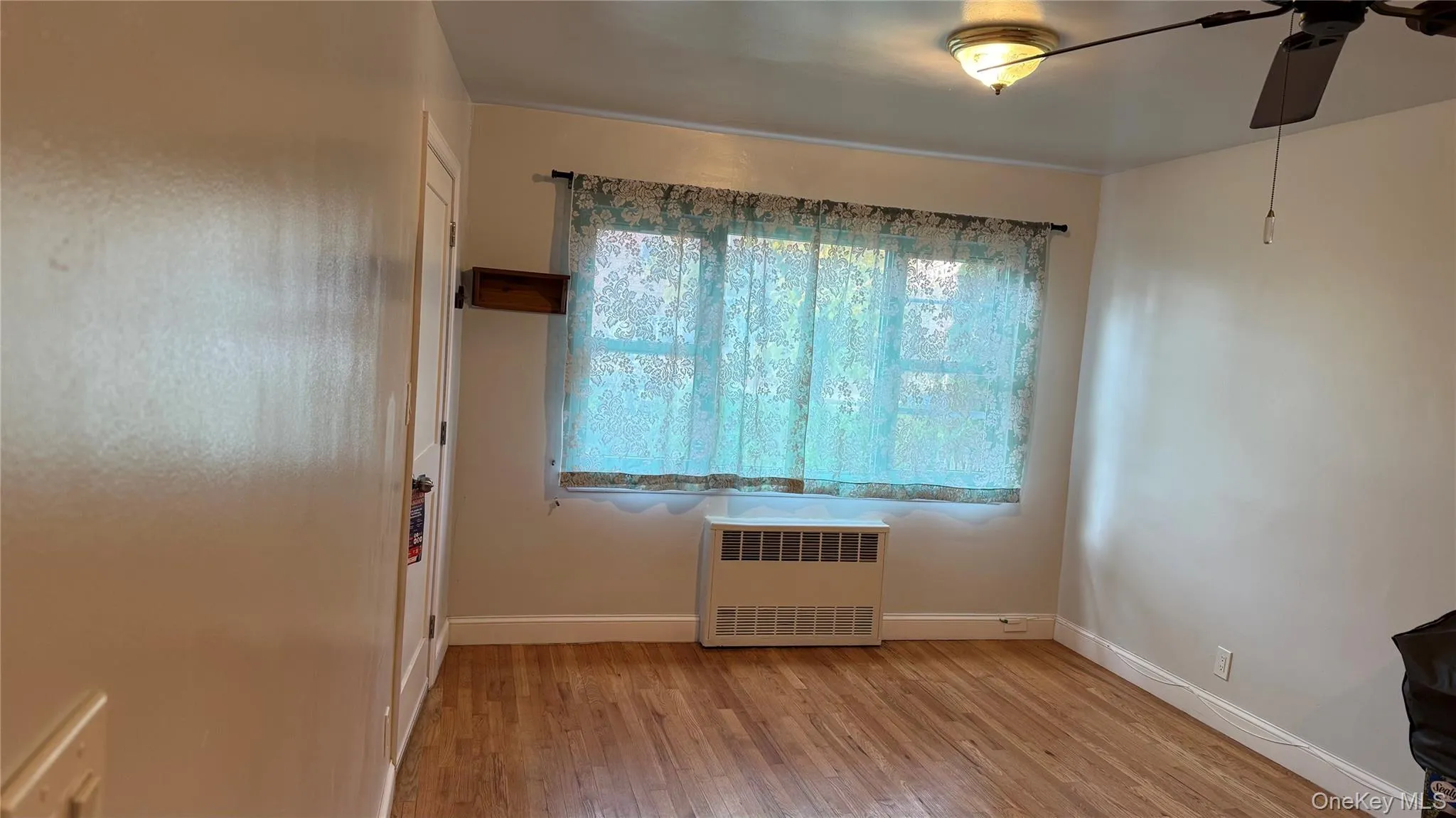 Unfurnished room with radiator, light wood-style flooring, and a ceiling fan Unfurnished room with radiator, light wood-style flooring, and a ceiling fan