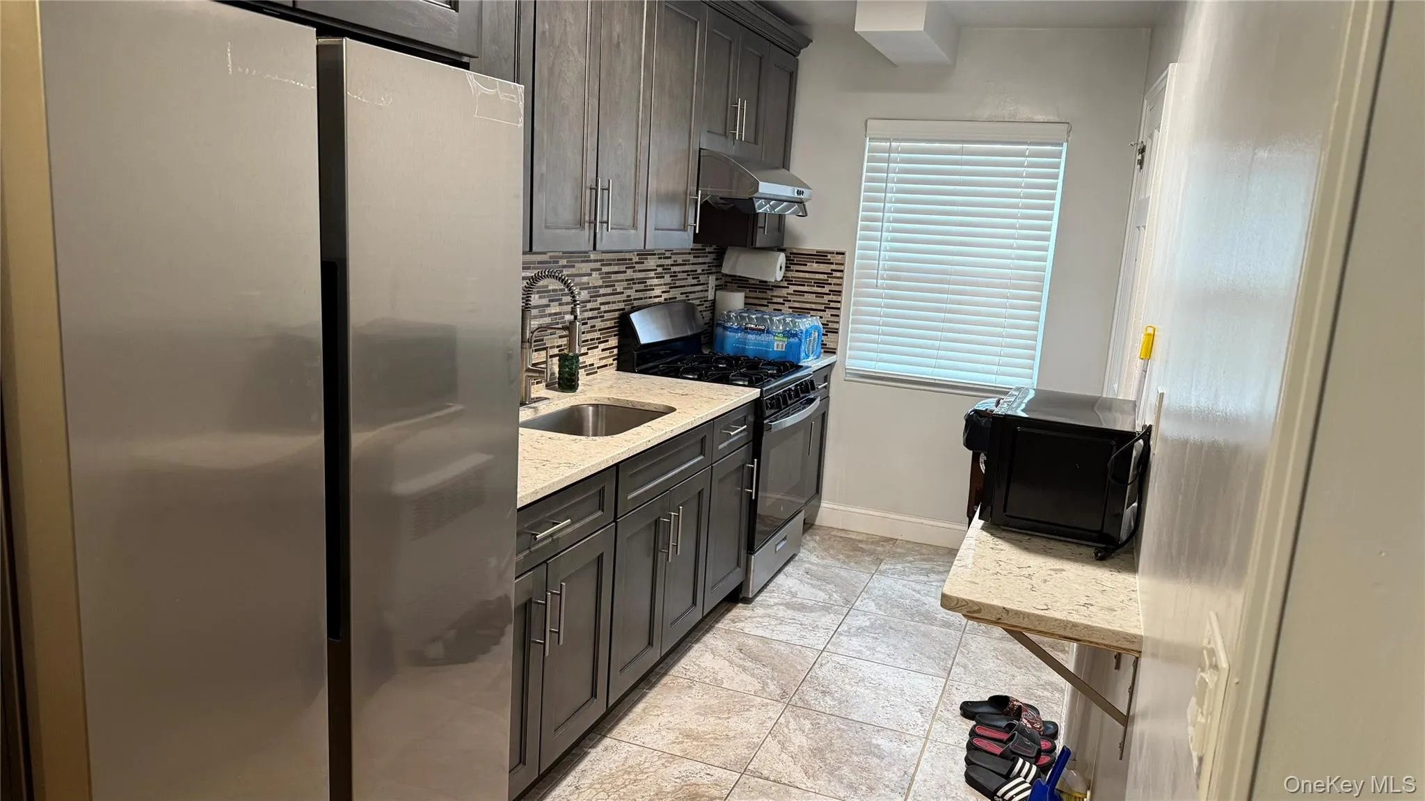 Kitchen with freestanding refrigerator, light stone countertops, gas stove, decorative backsplash, and black microwave Kitchen with freestanding refrigerator, light stone countertops, gas stove, decorative backsplash, and black microwave