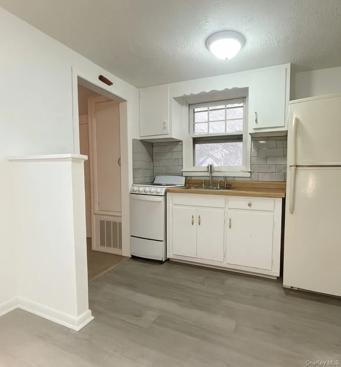 Kitchen with tasteful backsplash, white appliances, a textured ceiling, and white cabinetry Kitchen with tasteful backsplash, white appliances, a textured ceiling, and white cabinetry