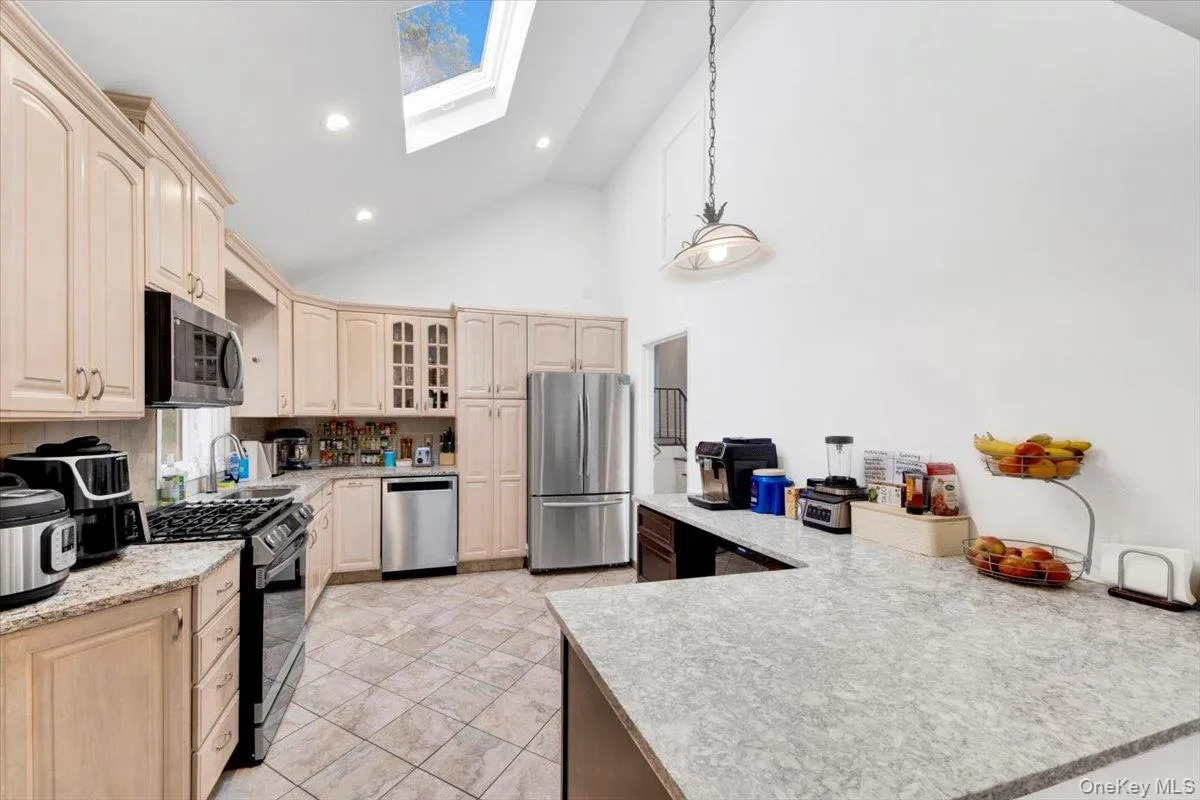 Kitchen with a skylight, stainless steel appliances, high vaulted ceiling, glass insert cabinets, and hanging light fixtures Kitchen with a skylight, stainless steel appliances, high vaulted ceiling, glass insert cabinets, and hanging light fixtures