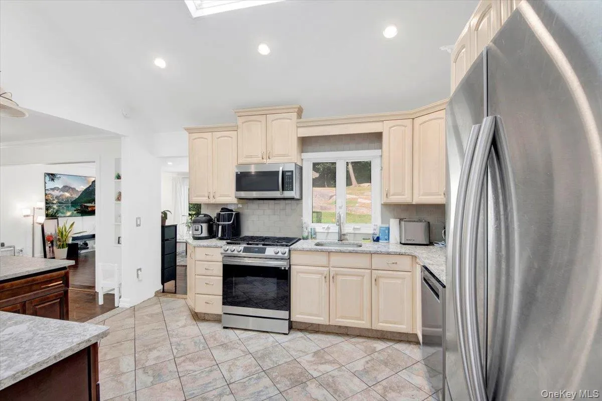 Kitchen featuring stainless steel appliances, recessed lighting, vaulted ceiling, backsplash, and a skylight Kitchen featuring stainless steel appliances, recessed lighting, vaulted ceiling, backsplash, and a skylight
