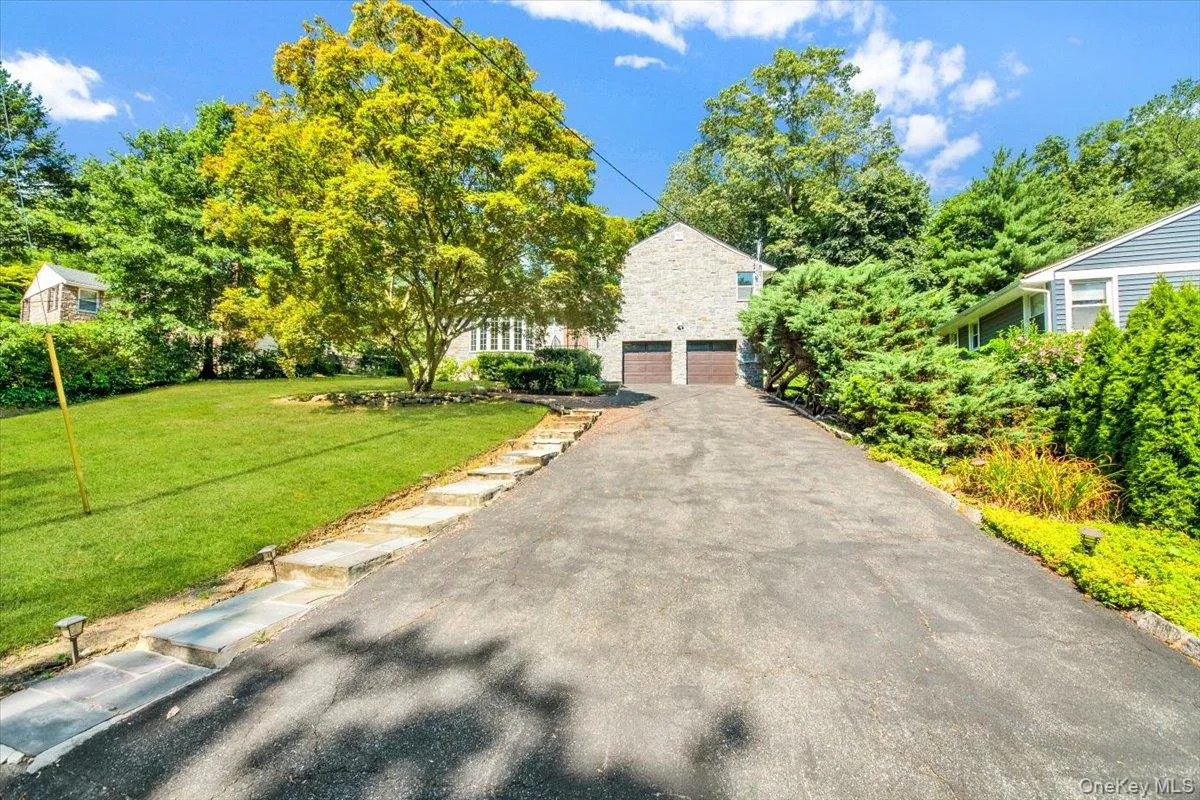 View of property hidden behind natural elements with a front lawn, driveway, and a garage View of property hidden behind natural elements with a front lawn, driveway, and a garage